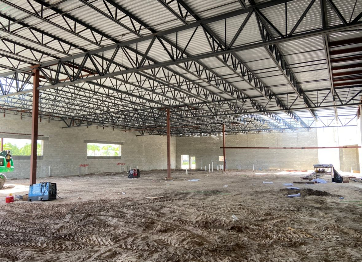 Interior view of a building under construction with exposed steel beams, concrete walls, and dirt floor.