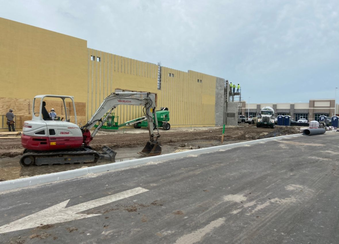 Construction site with an excavator, workers, and a large building.