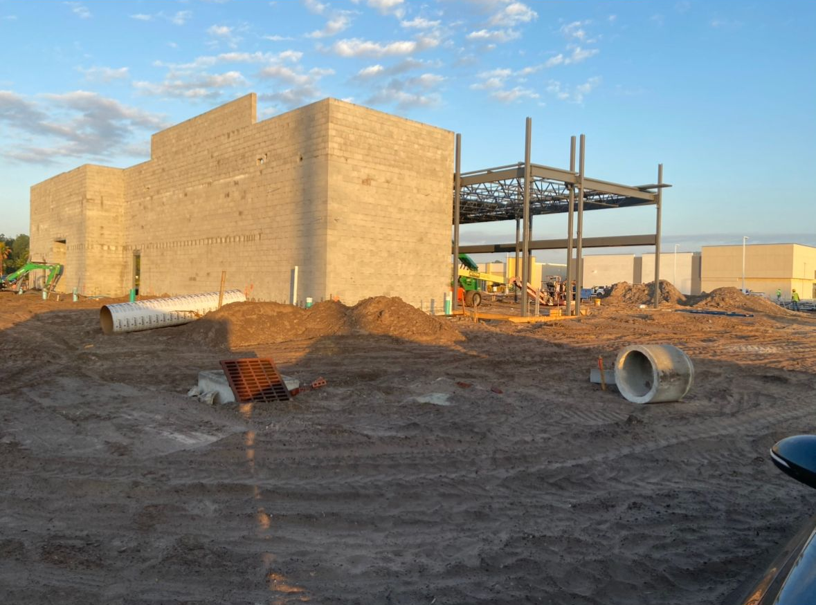 Construction site with concrete block building and steel framework against a blue sky.