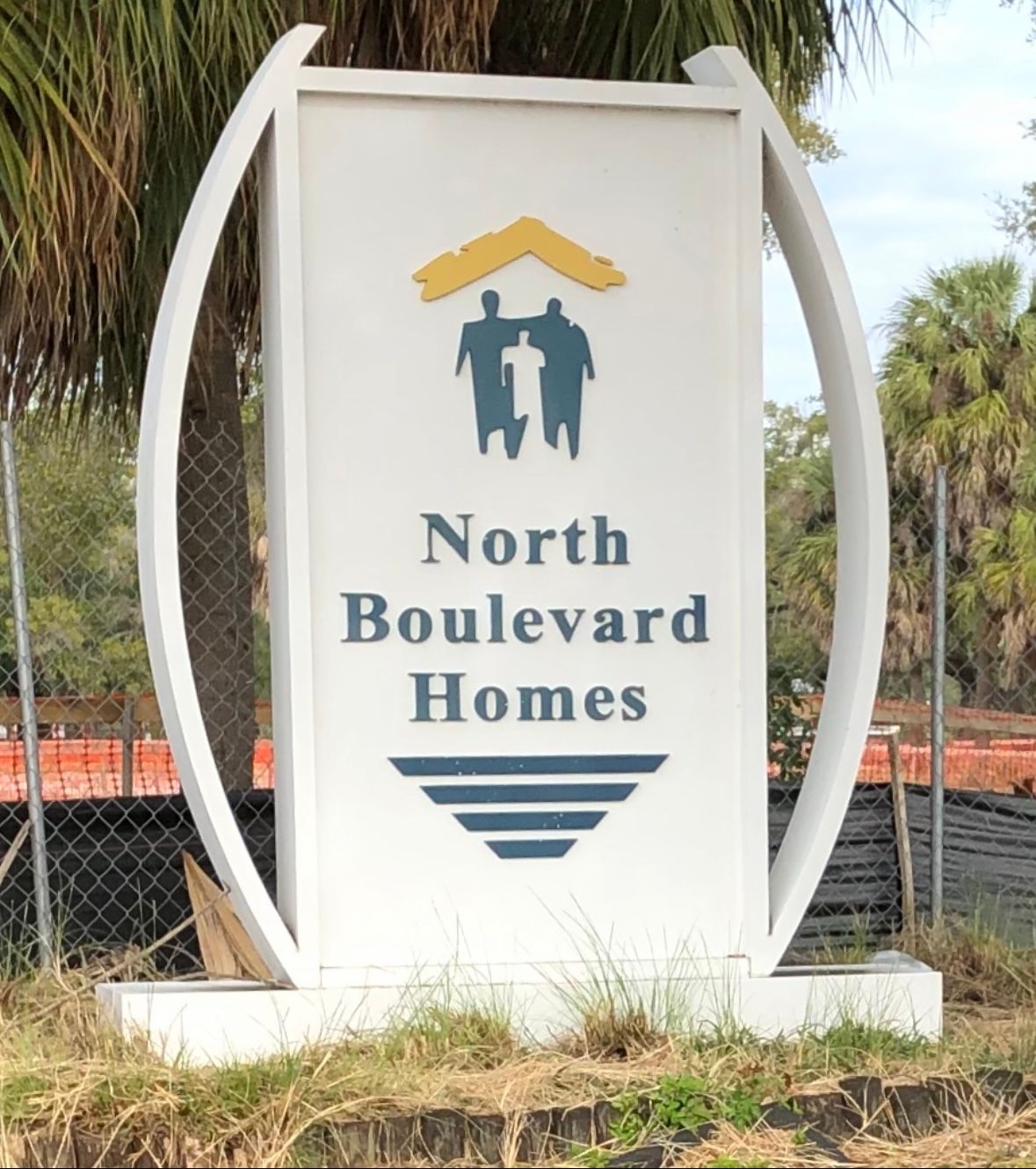 Sign for North Boulevard Homes: white with logo of family under roof. Blue text, stylized waves.