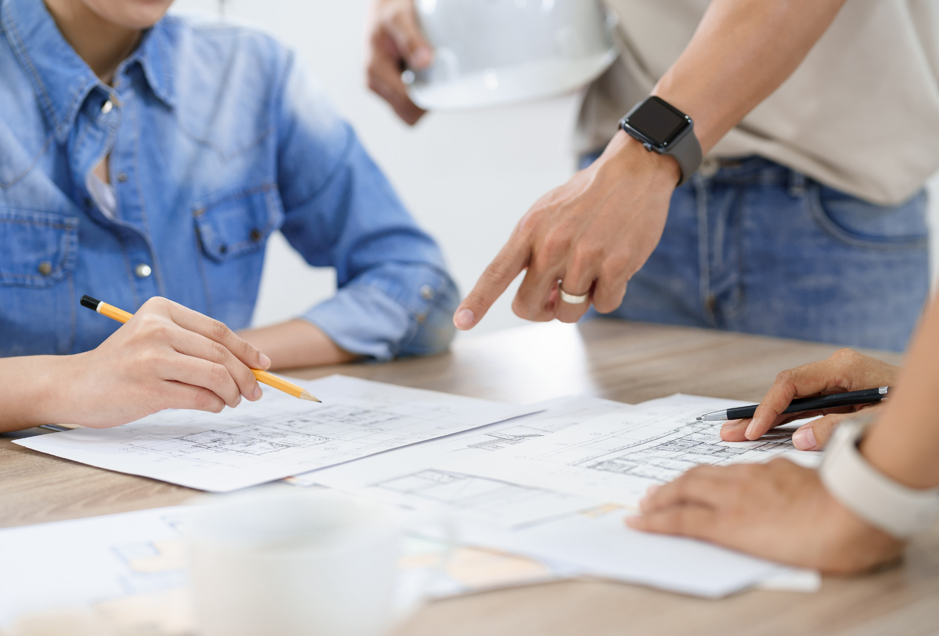People at a table reviewing blueprints, one pointing, another writing, and another holding a pen.