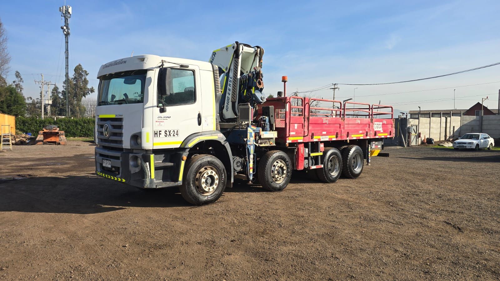 Un gran camión de plataforma blanco y rojo con una grúa estacionado en un lote de grava.