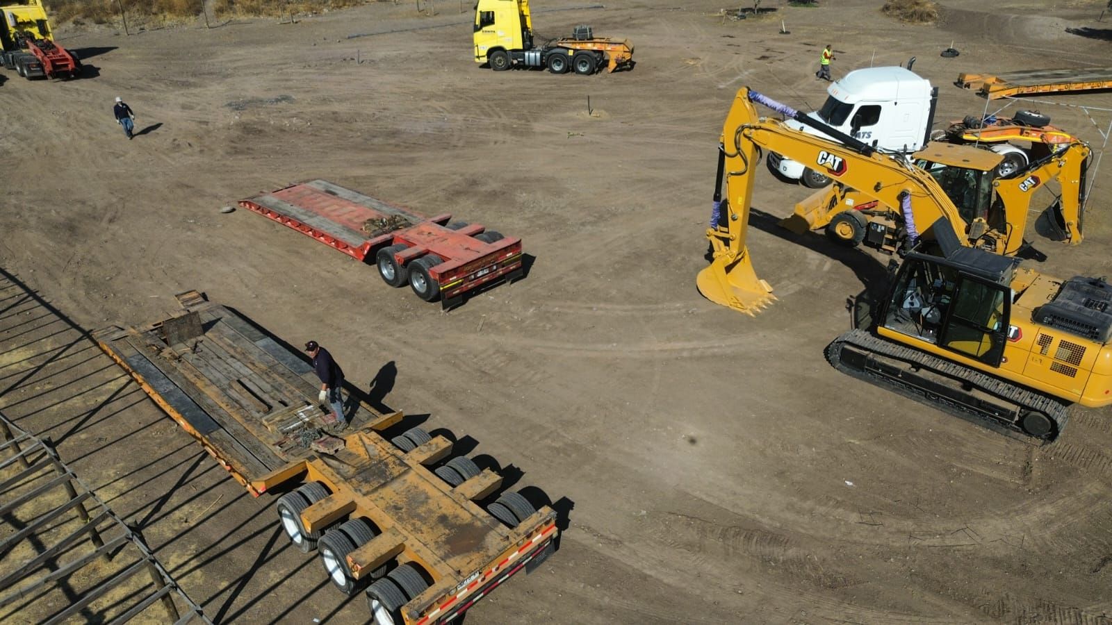 Una obra en construcción con una excavadora amarilla, camiones