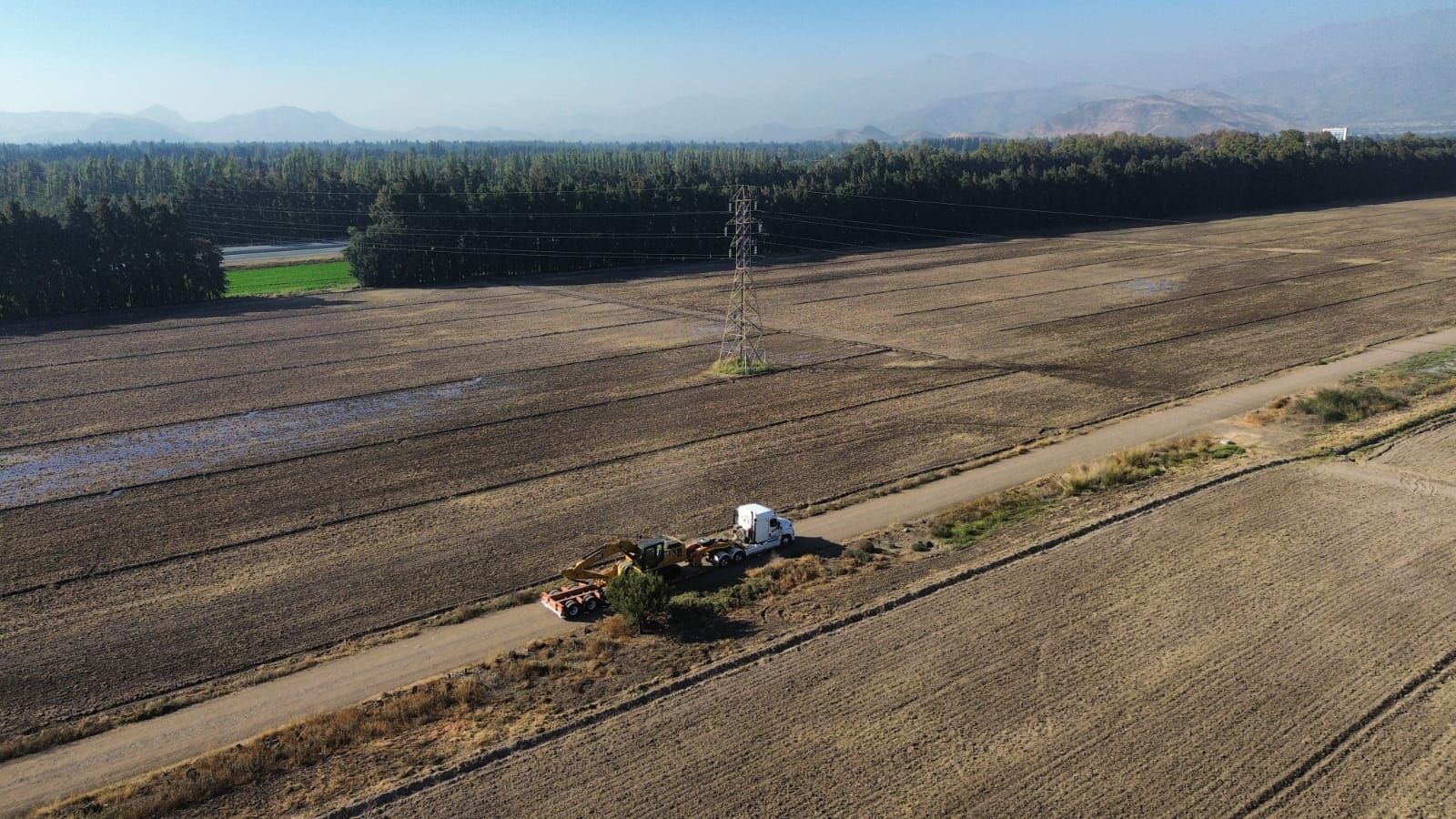 Vista de dron de un camión y árboles en un campo, con montañas en la distancia.