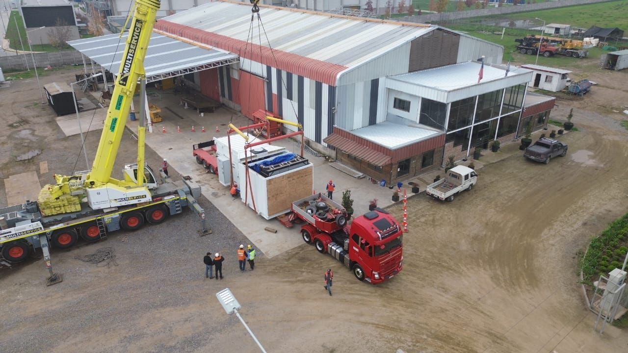 Una grúa levanta una gran estructura rectangular desde un camión en un edificio industrial.