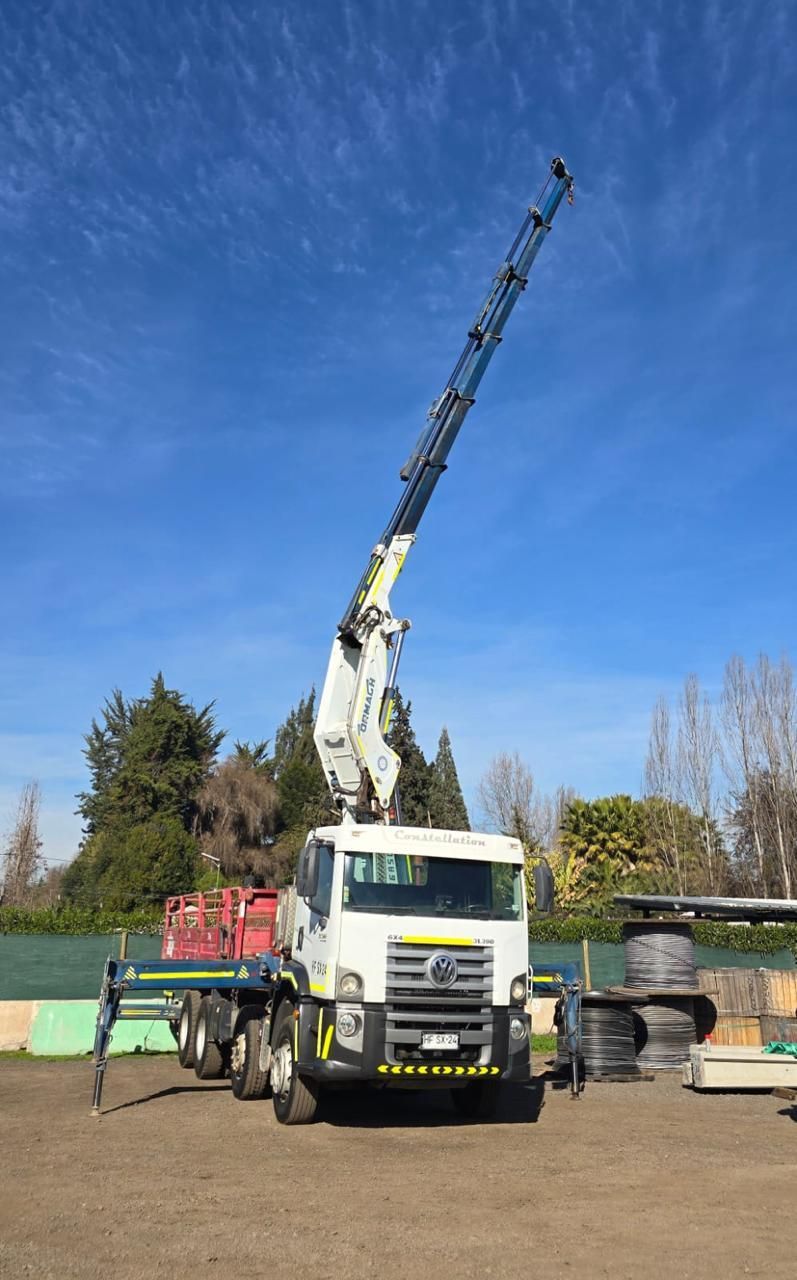 Grúa montada en camión con la pluma extendida contra un cielo azul. El camión, blanco y amarillo, está estacionado al aire libre.