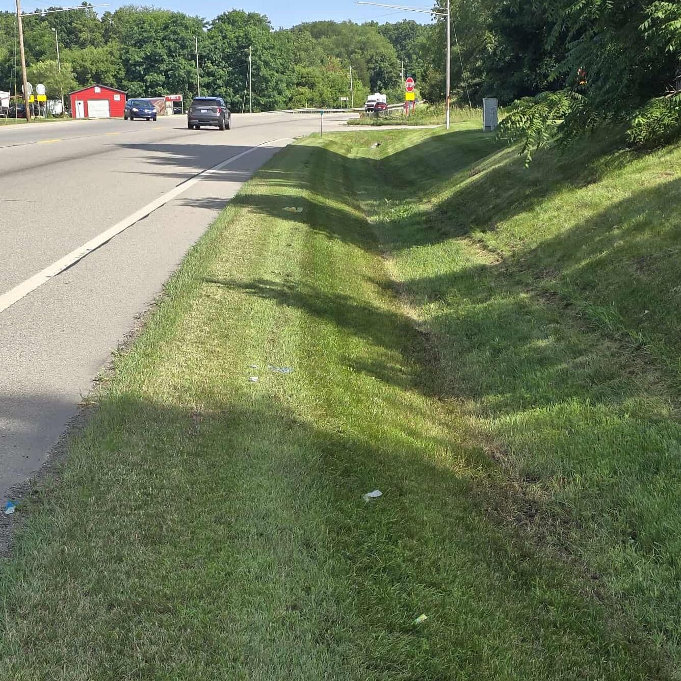 A car is driving down a road next to a grassy hill.