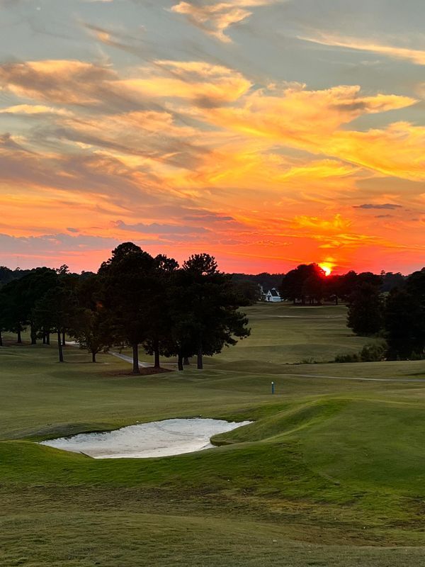 The sun is setting over a golf course with a sunset in the background.