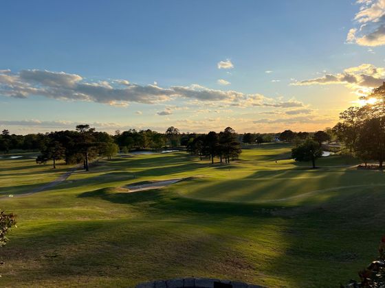 The sun is setting over a golf course with trees in the background.