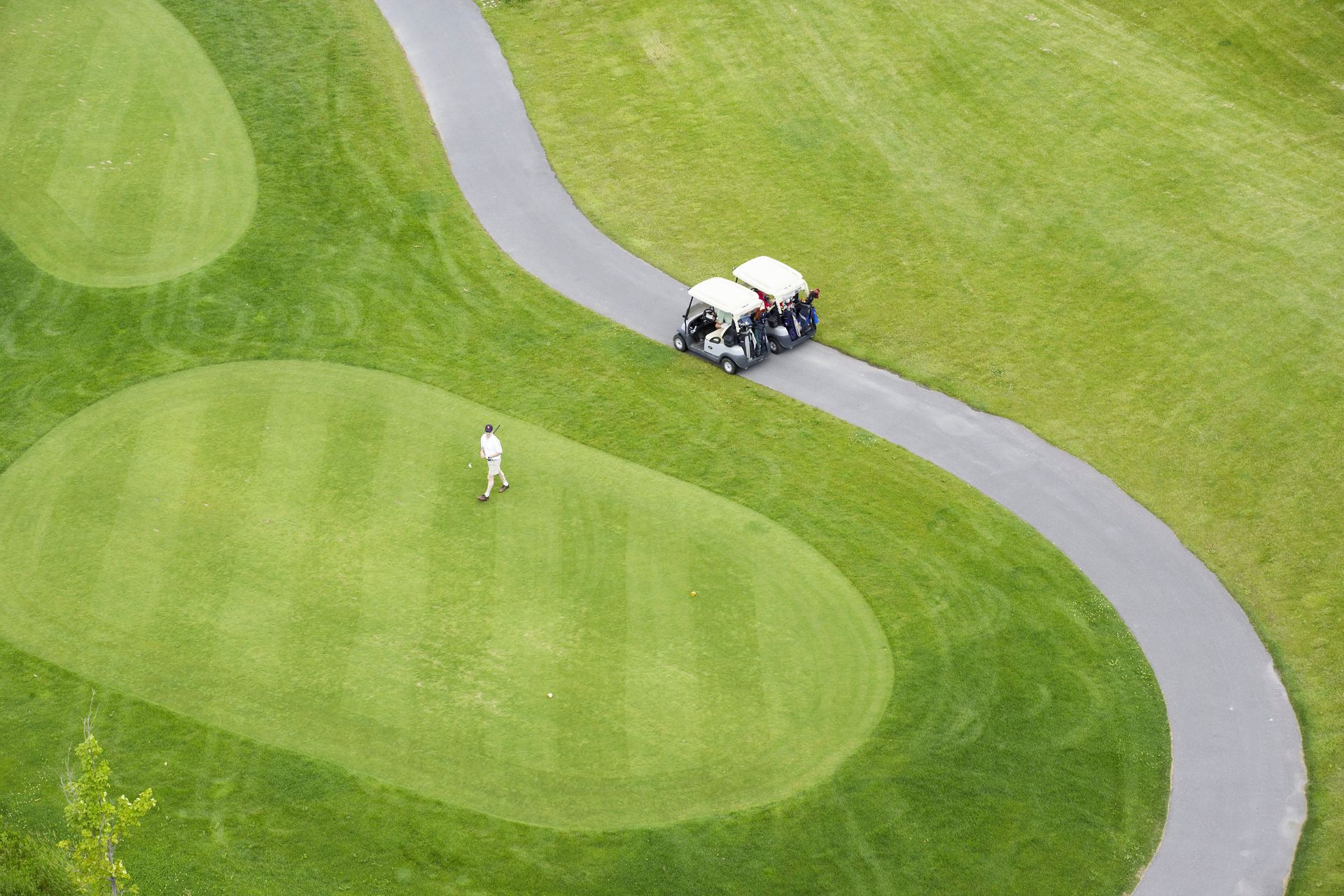 An aerial view of a golf course with a golf cart driving down the road.