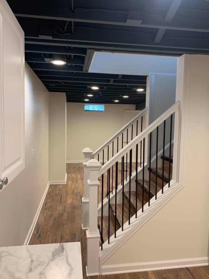 Basement with stairs, white walls, black ceiling, and wood-look flooring.
