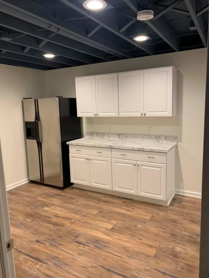 Kitchenette with white cabinets, stainless steel fridge, and wood-look flooring in a room with a dark blue ceiling.