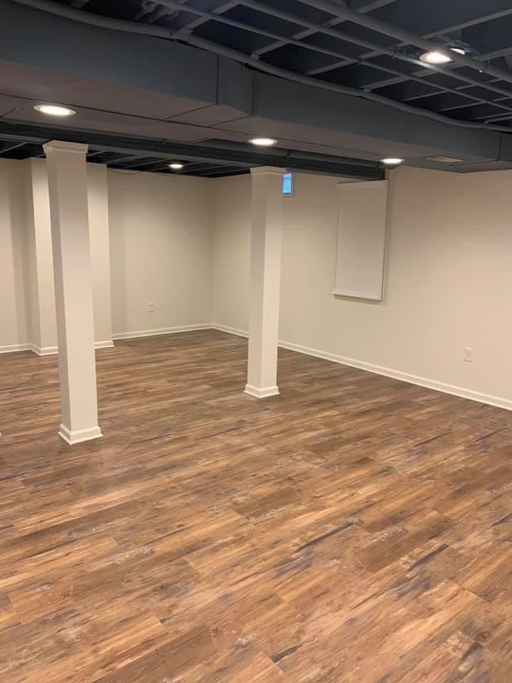 Basement with wood-look flooring, white pillars, and a dark blue ceiling with recessed lights.