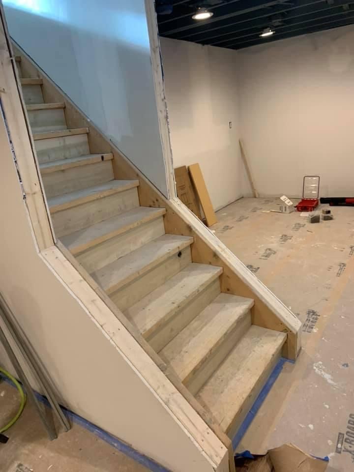 Staircase in a room under construction, wooden steps with drywall on walls.