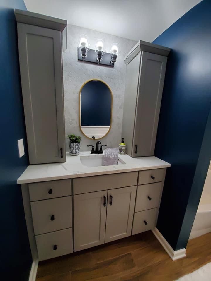Gray bathroom vanity with cabinets, oval mirror, and blue walls.