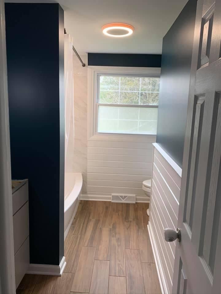 Bathroom with navy blue walls, white shiplap, wood-look tile, and modern ceiling light.