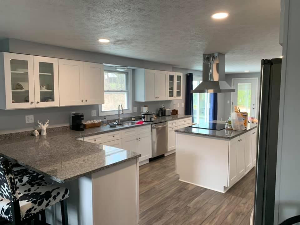 Bright and clean white kitchen with granite countertops, a central island with a custom range hood, and featuring Shaker cabinets, stainless steel appliances and new LVP flooring.