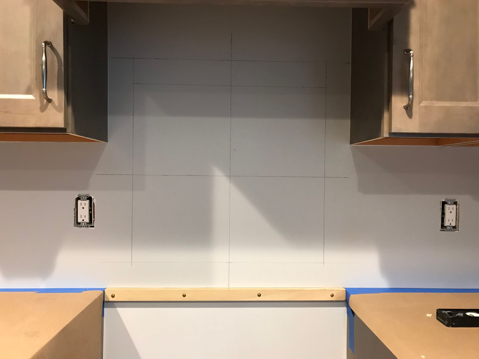 Wall marked for tile backsplash between kitchen cabinets and countertops.