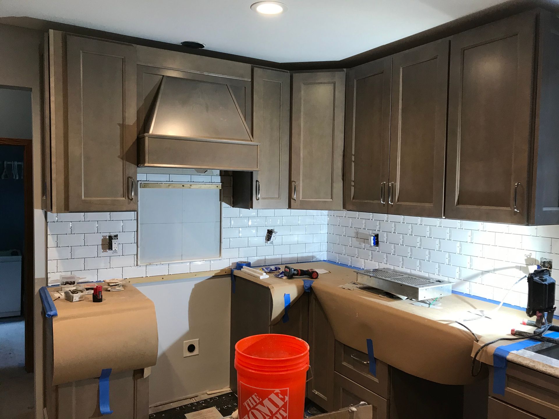 Kitchen under construction: gray cabinets, white subway tile backsplash, orange Home Depot bucket on counter.