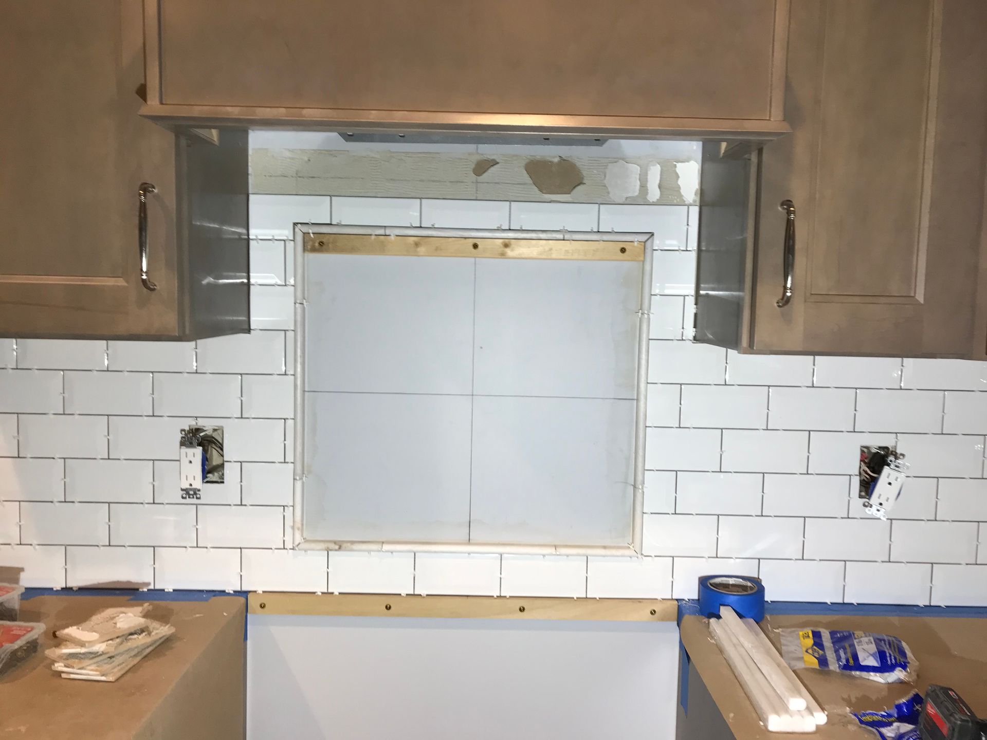 Kitchen backsplash with white subway tiles, unfinished hood vent, and upper cabinets.