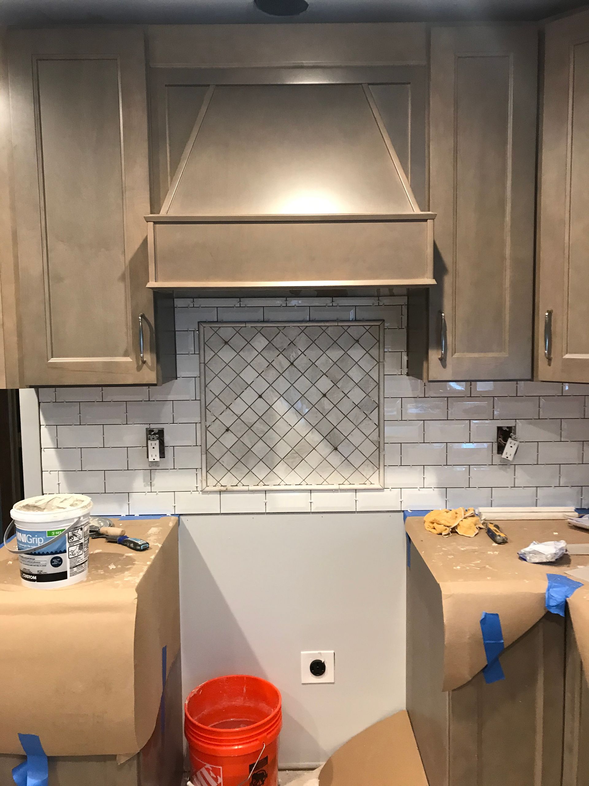 Kitchen with beige cabinets, tile backsplash, range hood, and prep work on the countertop.