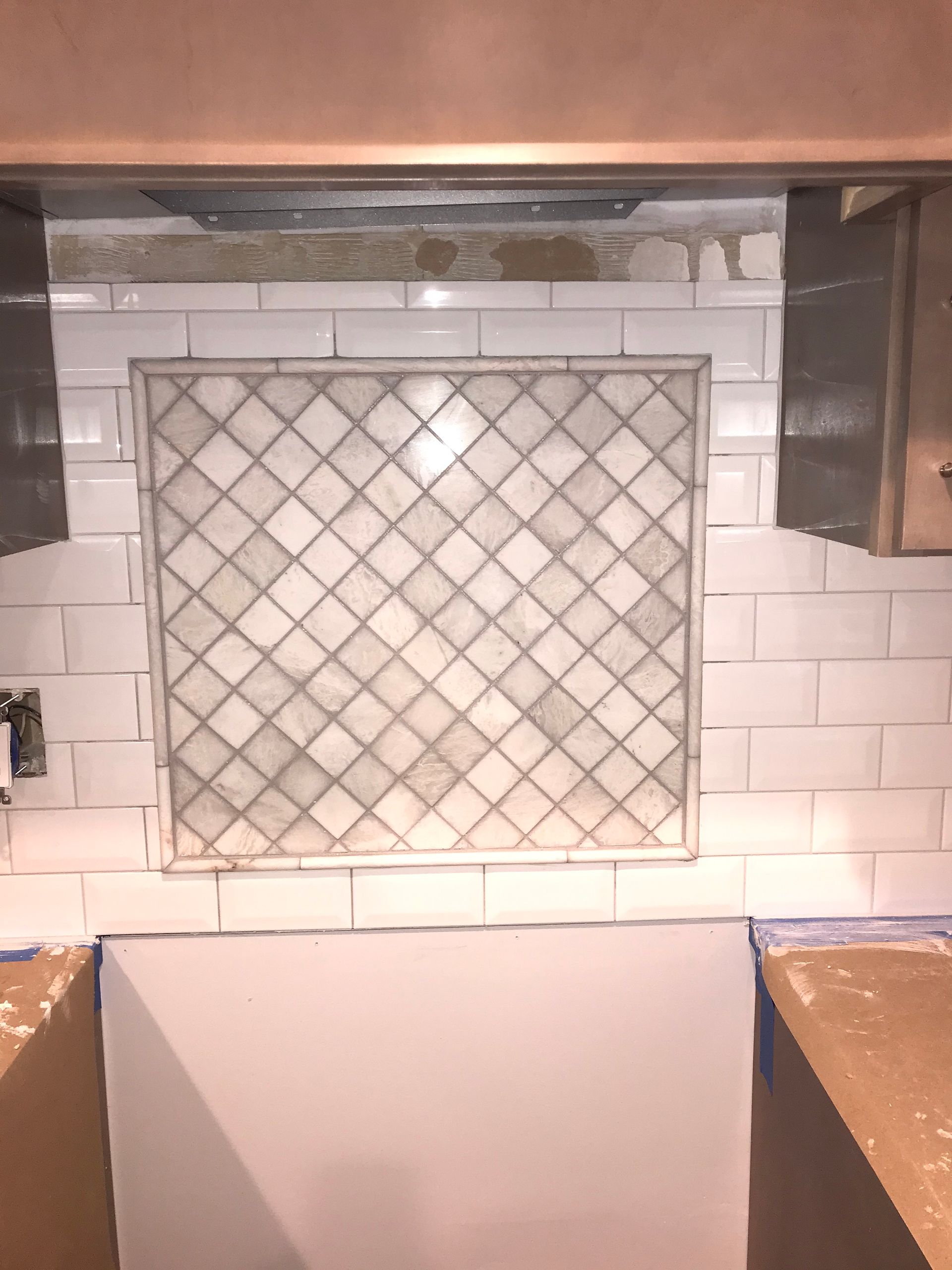 Kitchen backsplash under construction with diamond-patterned tile feature surrounded by white subway tiles.