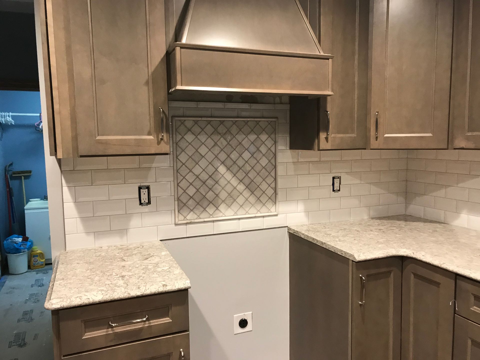 Kitchen with gray cabinets, white tile backsplash, stainless steel hood, and granite countertops.