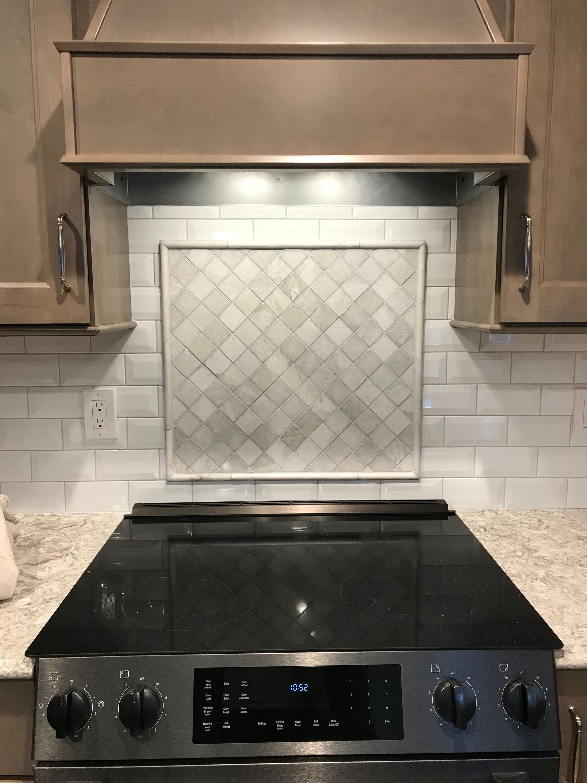Kitchen stove with a patterned tile backsplash, and a range hood.