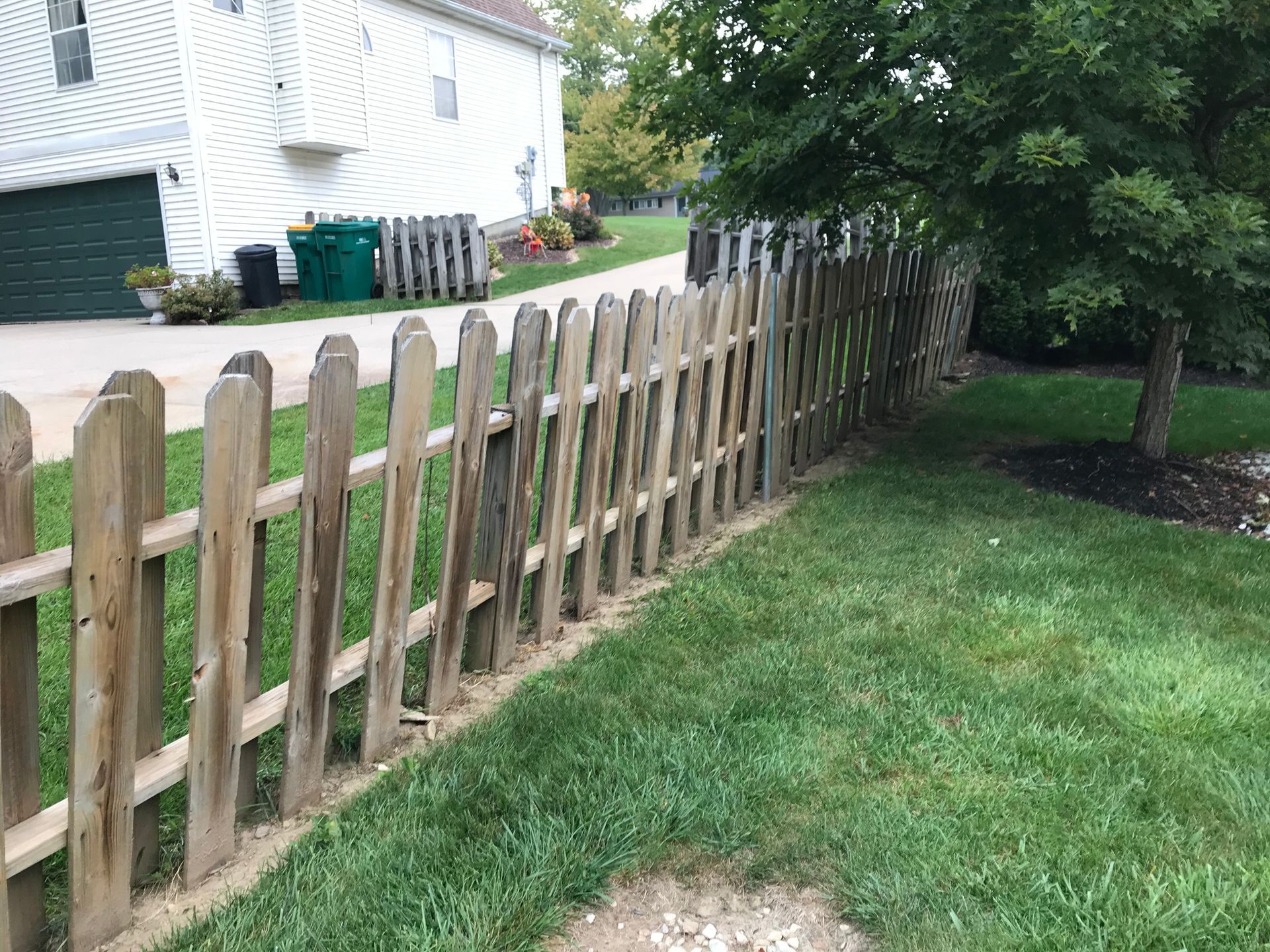 Wooden picket fence along a grassy yard, near a tree and a white house.