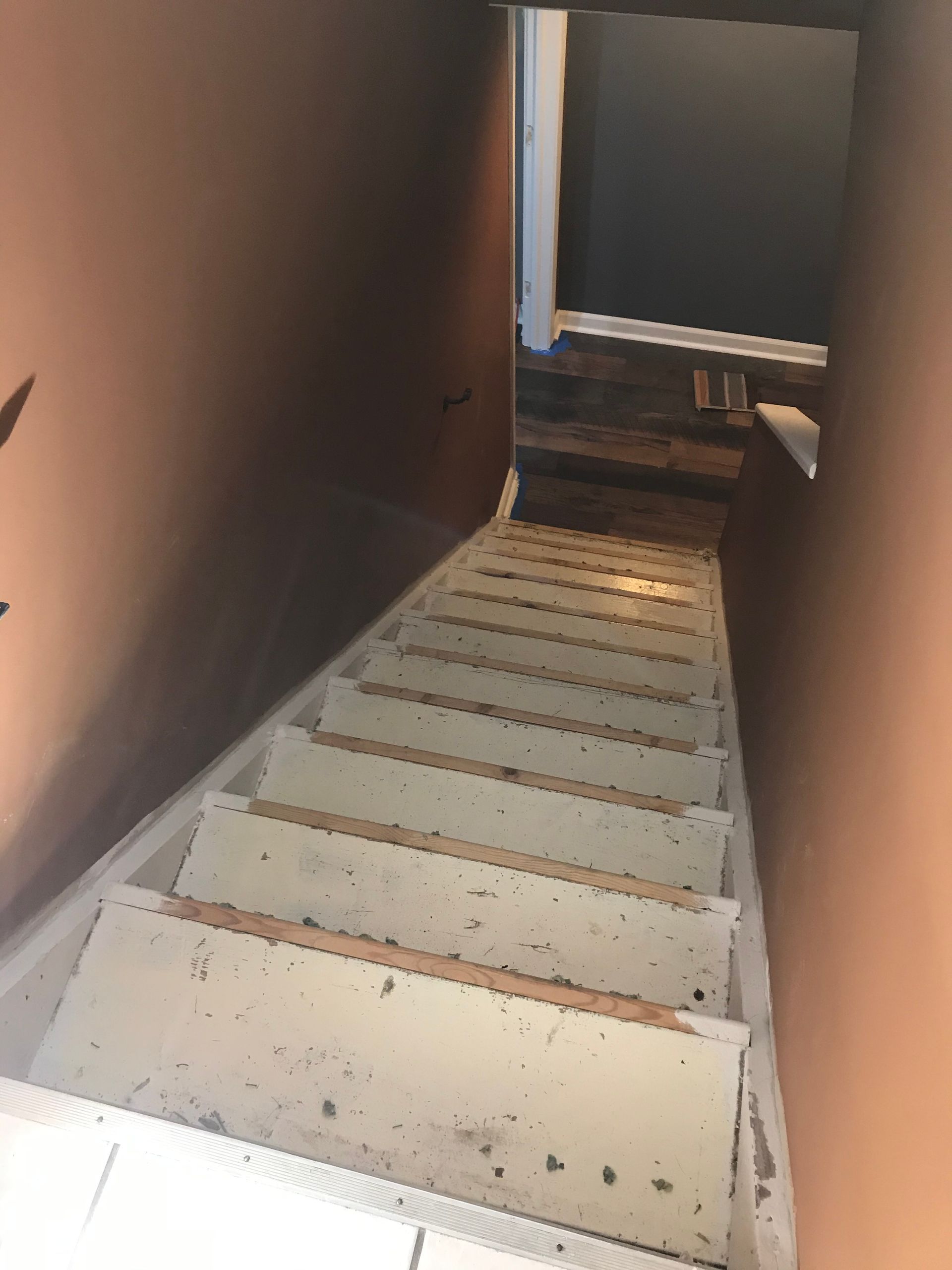 Downward view of a white staircase between orange walls, leading into a dimly lit area.