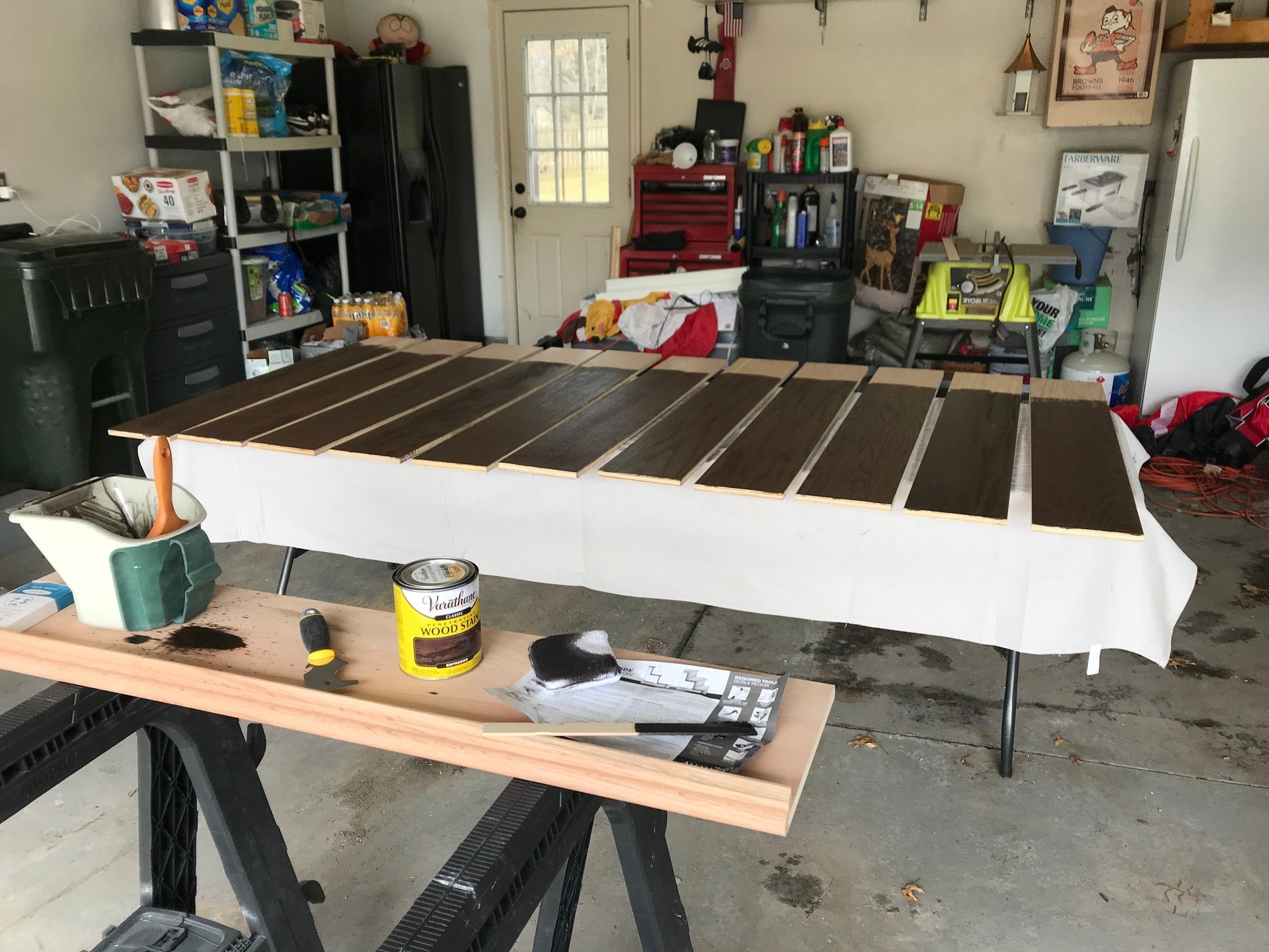 Wooden planks laid out and stained in a garage, with paint supplies visible.