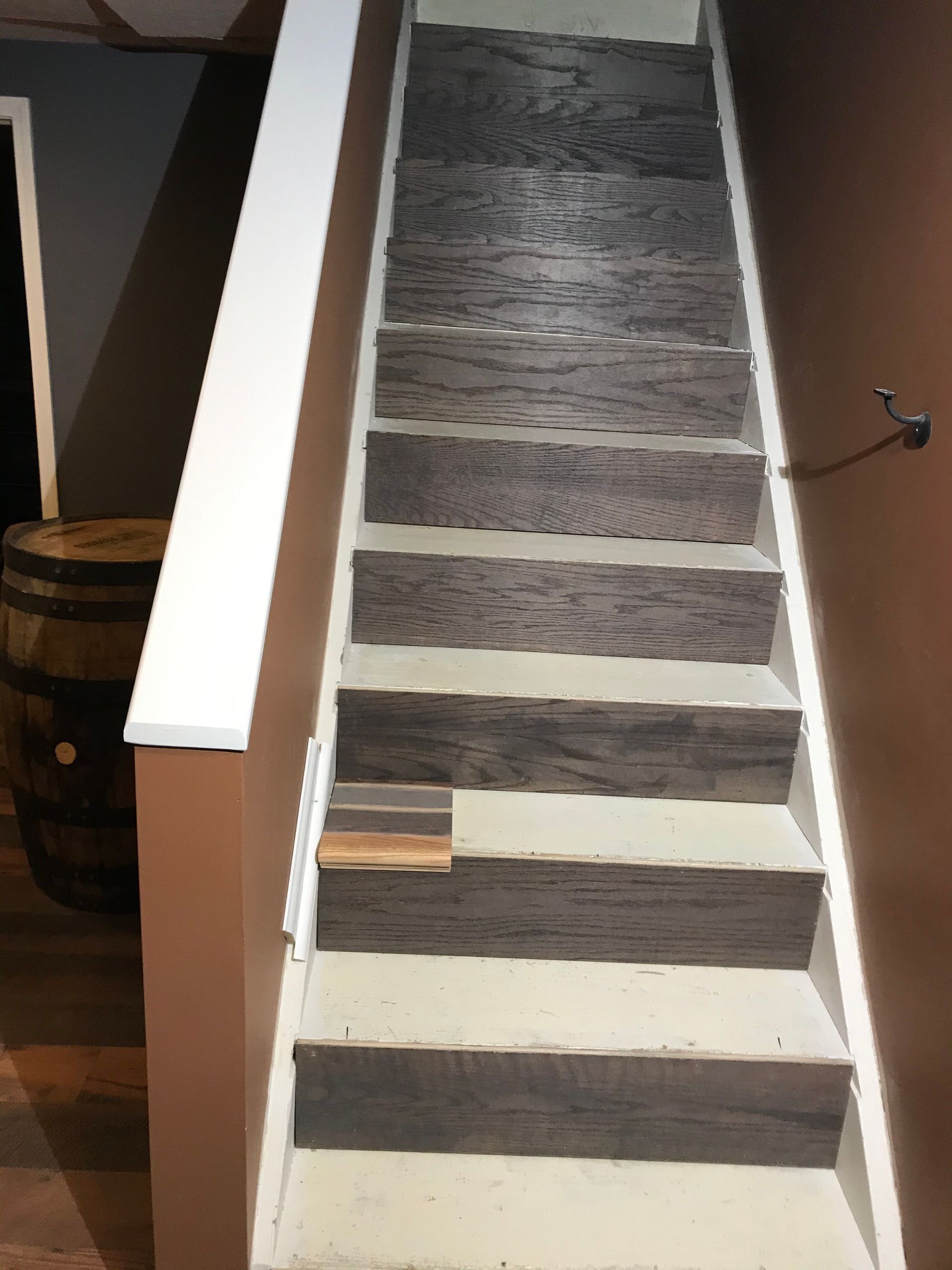 Wooden steps with distressed planks, white risers, brown walls, and a barrel to the left.