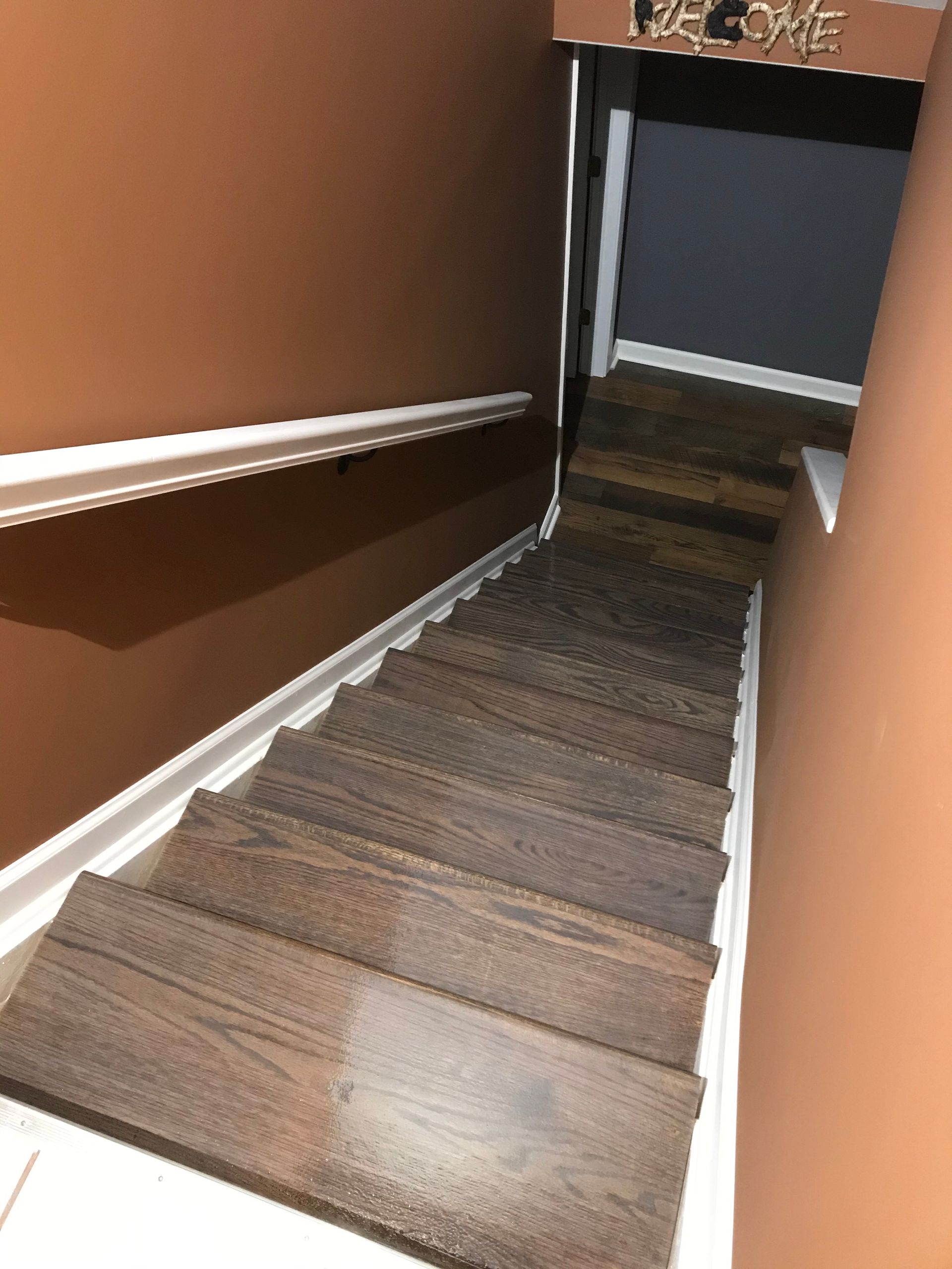 Staircase leading down with brown treads, brown walls, and white trim, with 
