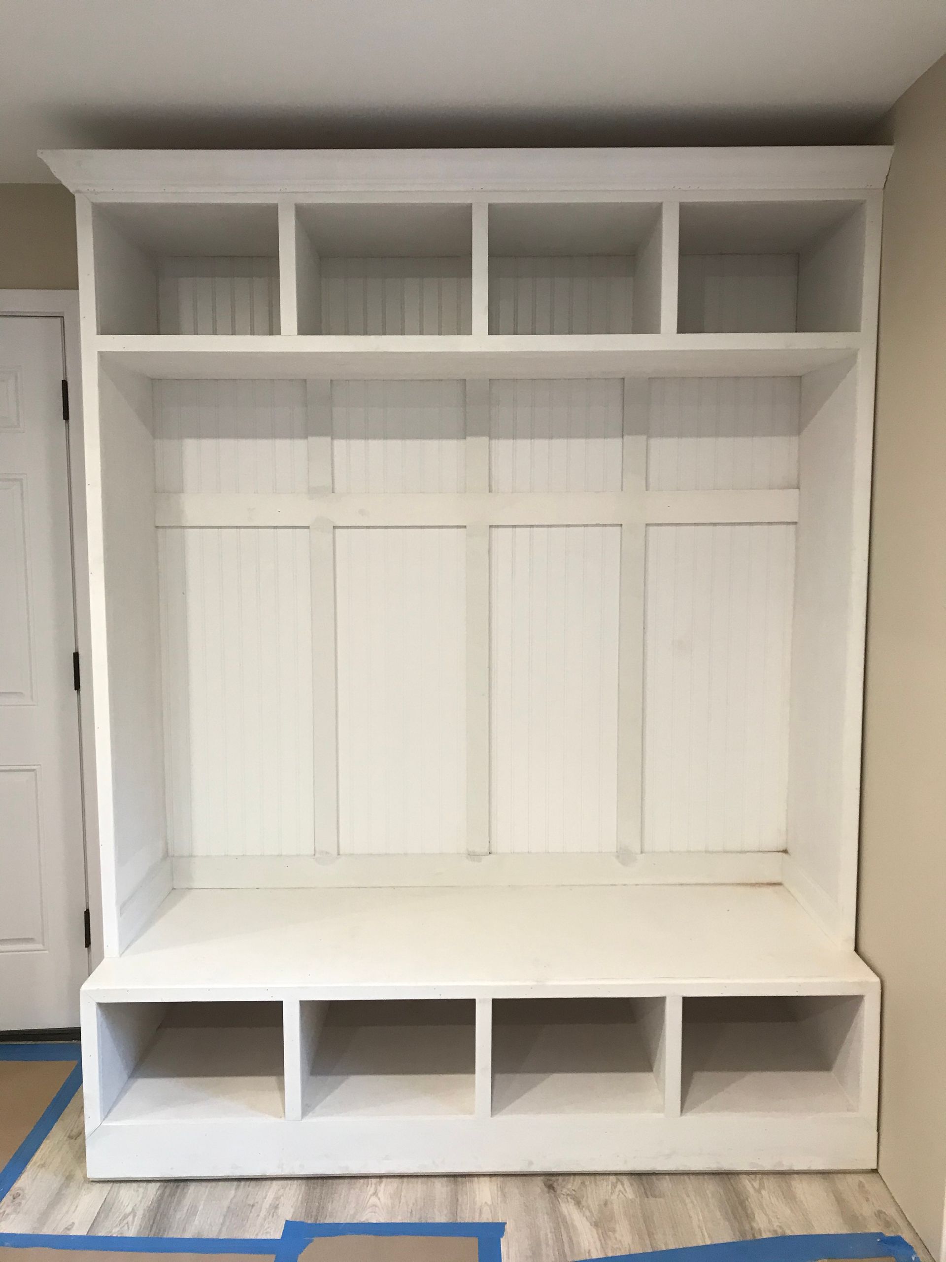 White built-in entryway unit with overhead storage, vertical panels, bench, and lower cubbies.