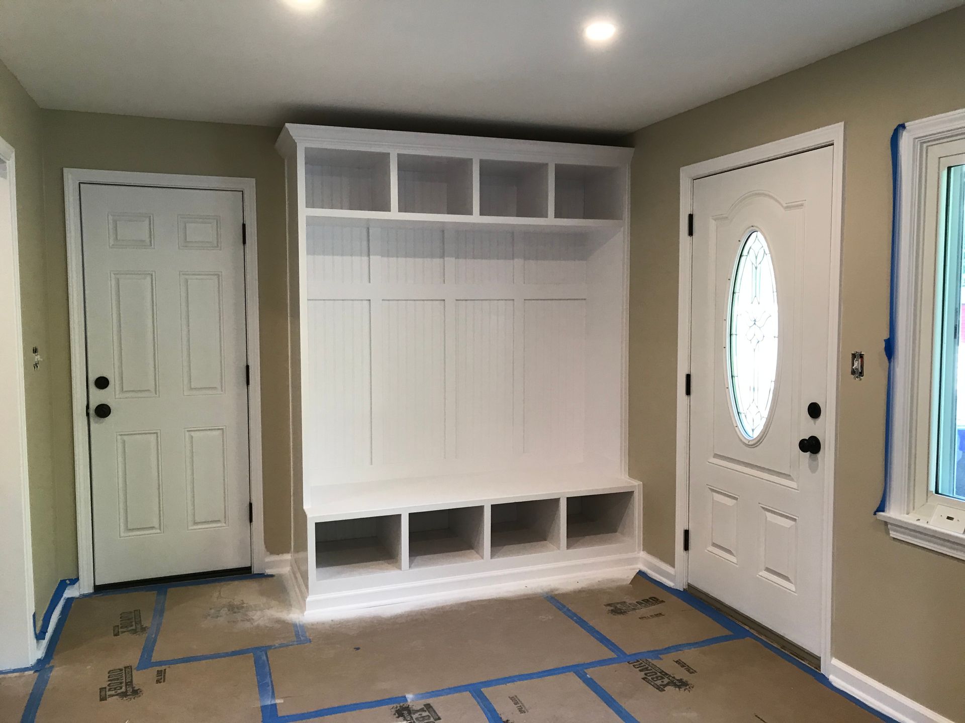 White entryway with built-in bench, cubbies, and storage, between two doors.