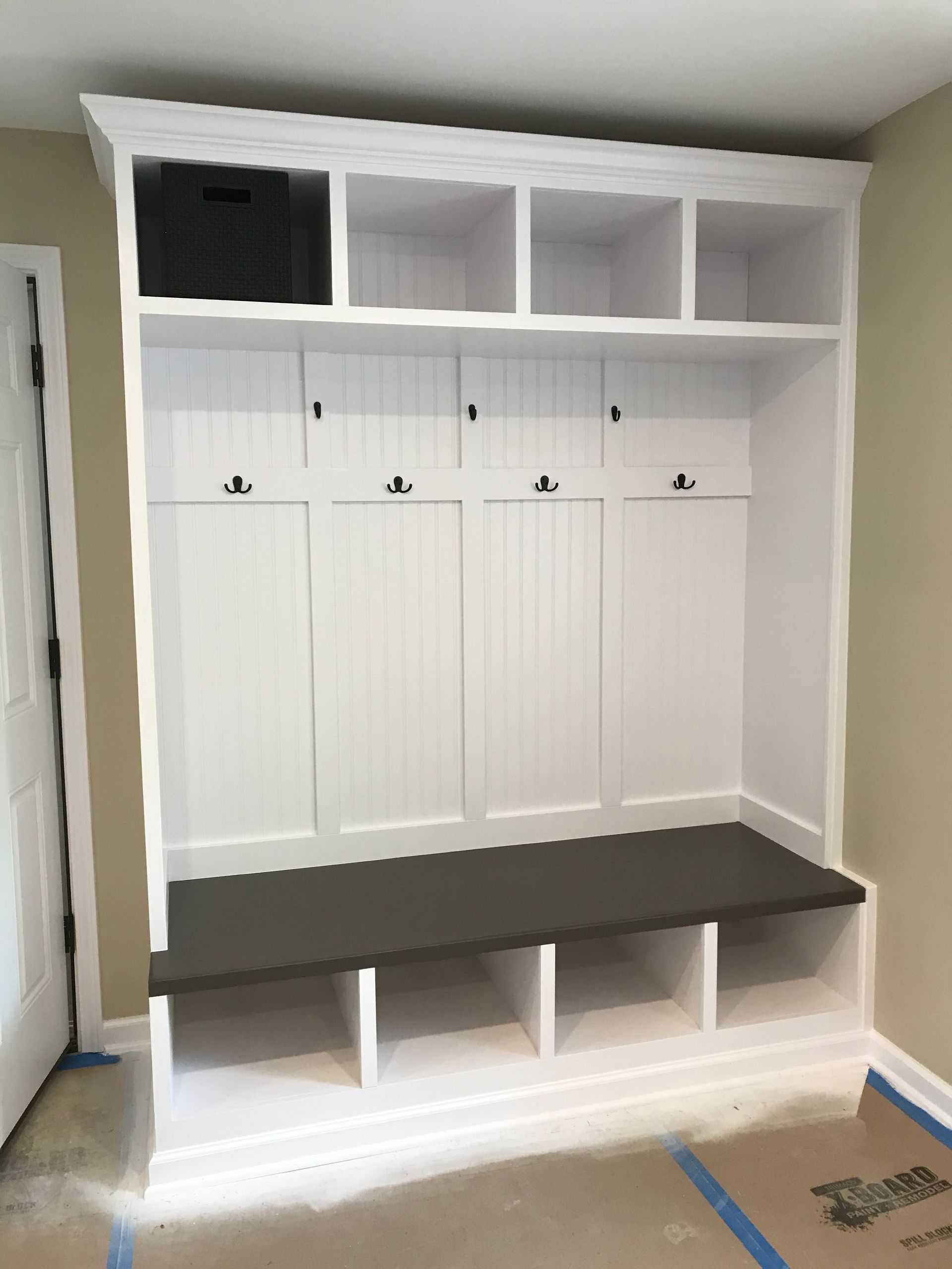 White built-in mudroom storage with cubbies, hooks, and a bench; gray bench cushion.