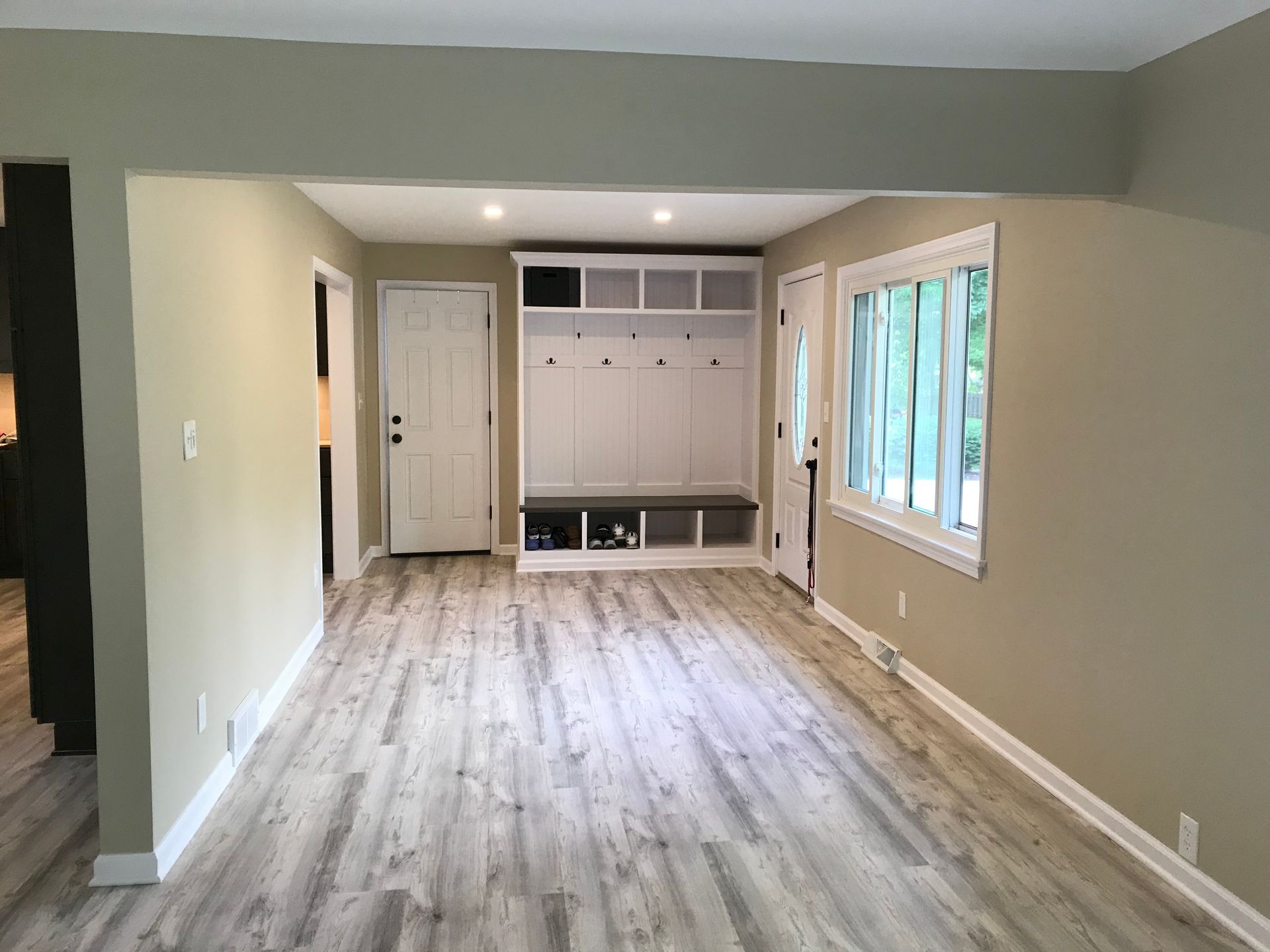 Empty interior with light wood floors, tan walls, white trim, and a built-in mudroom.