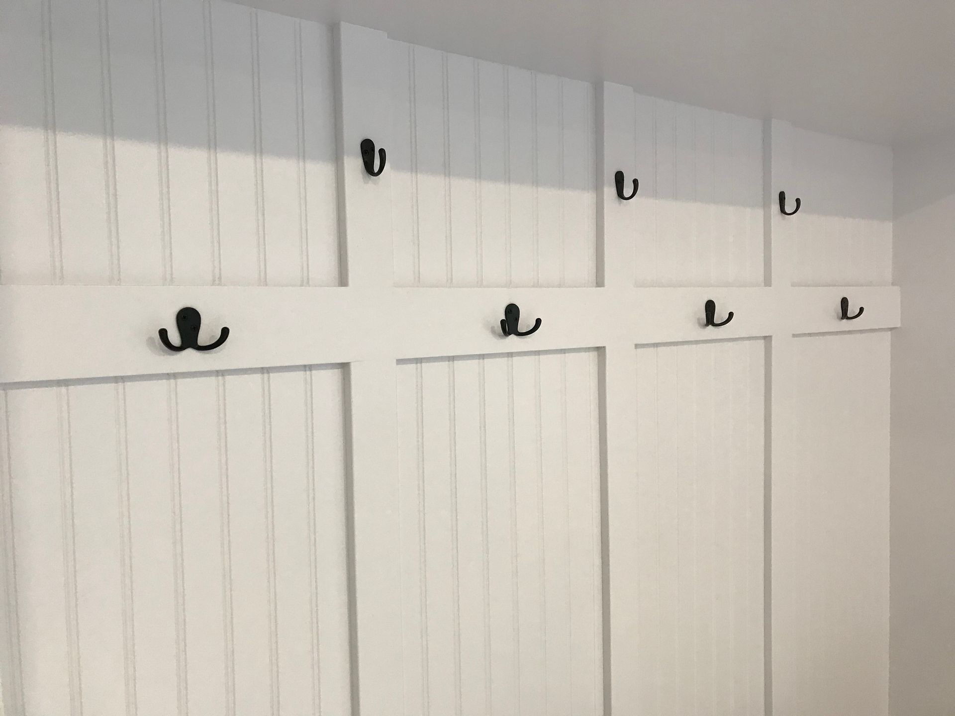 White paneled wall with black coat hooks.