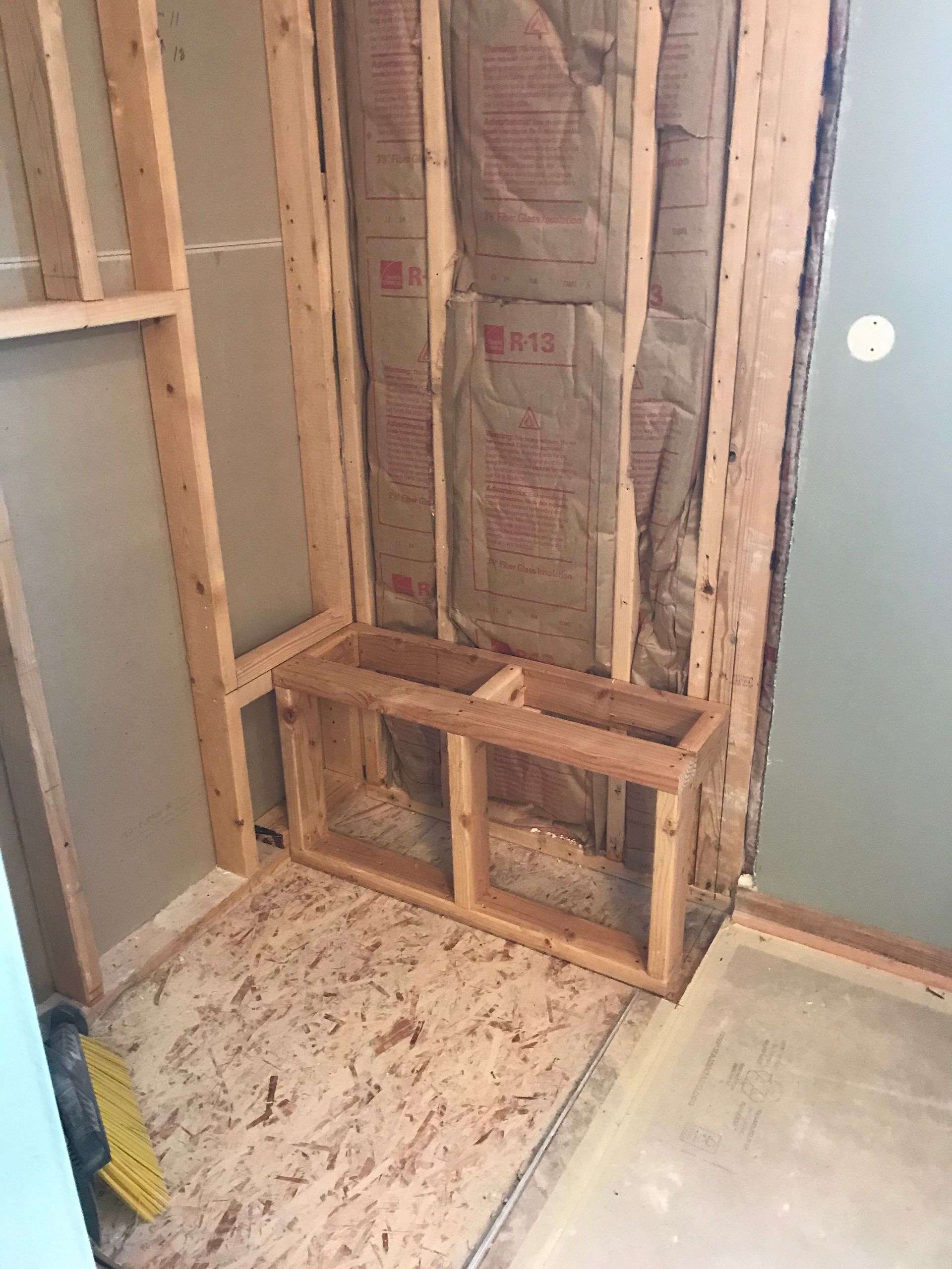 Framed bathroom construction, wooden shelving built-in, insulation visible, and wood-framed walls.