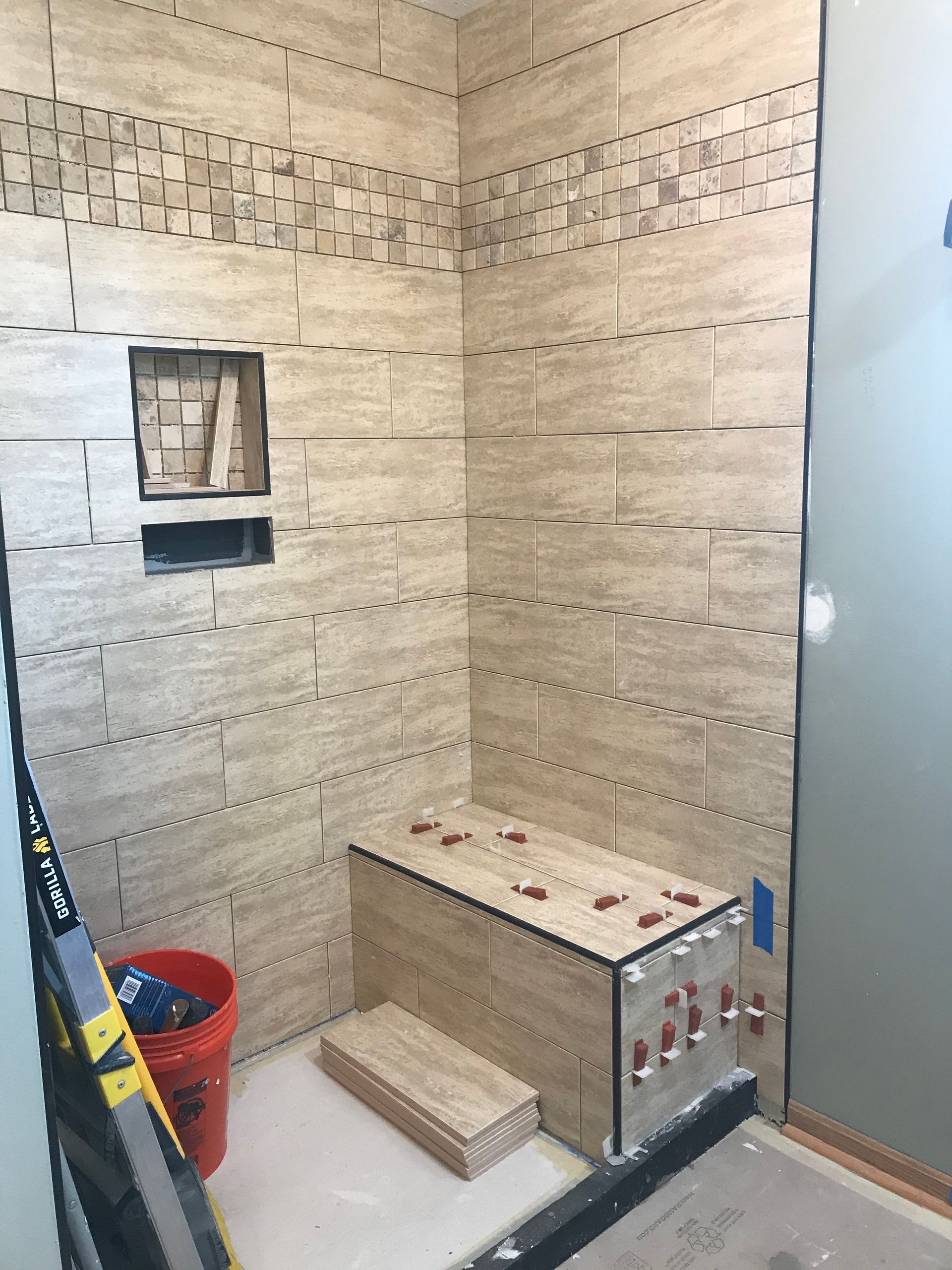 Shower stall under construction with beige tiles, bench, and recessed shelf.