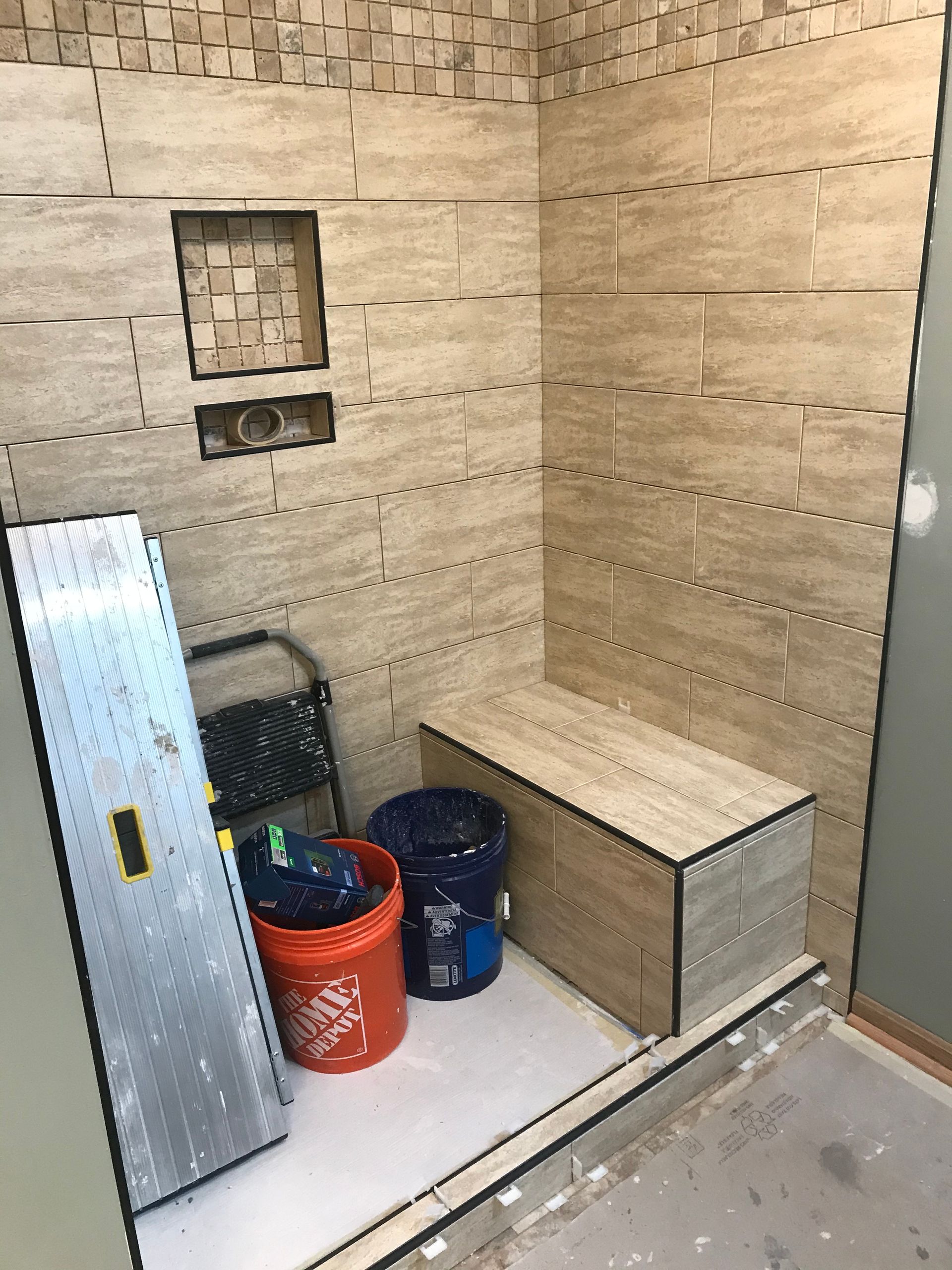 Shower stall under construction with tiled walls and a built-in bench; tools and buckets present.
