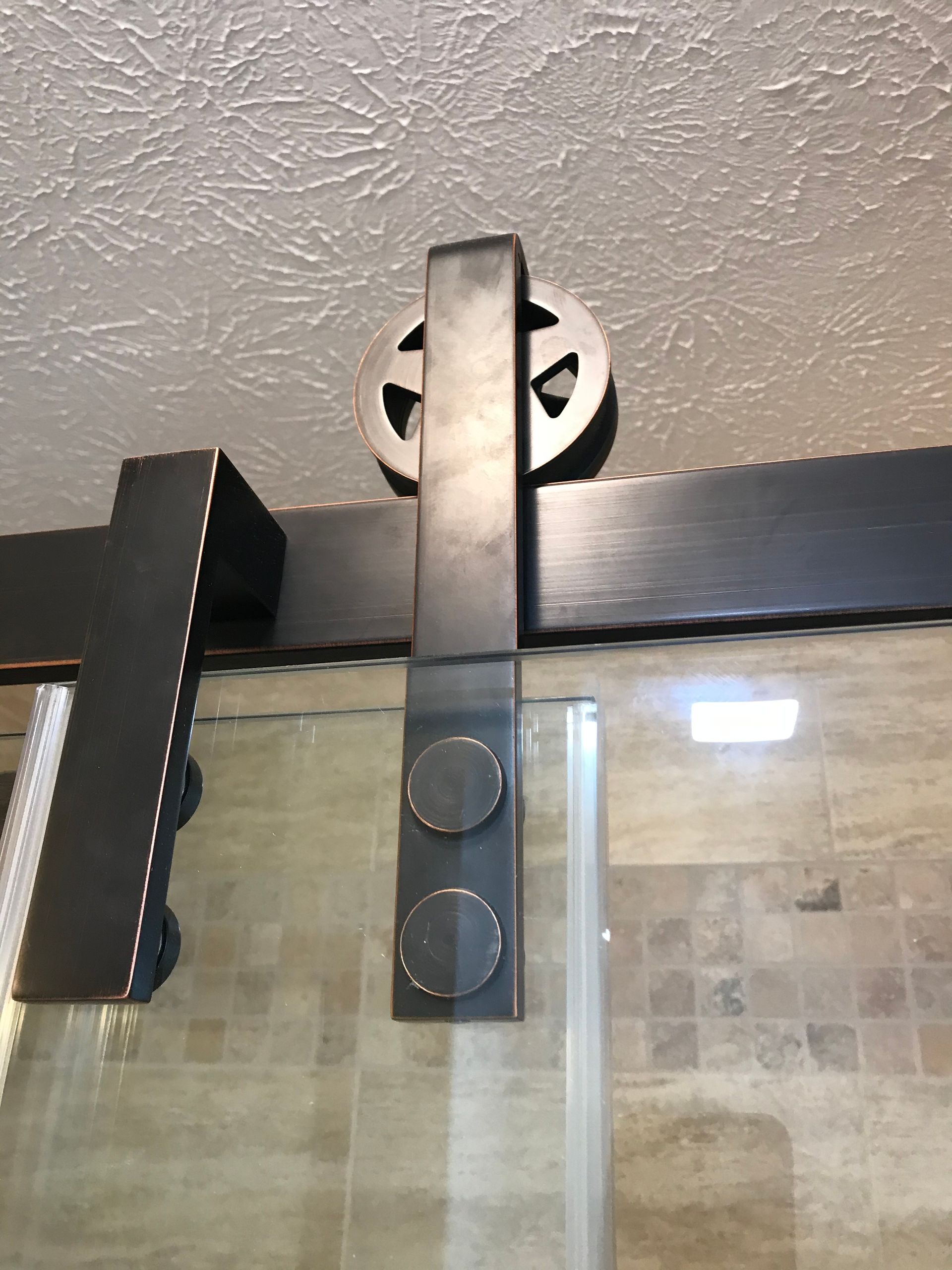 Barn door hardware with a star-shaped wheel, mounted on a dark track, over a glass door.