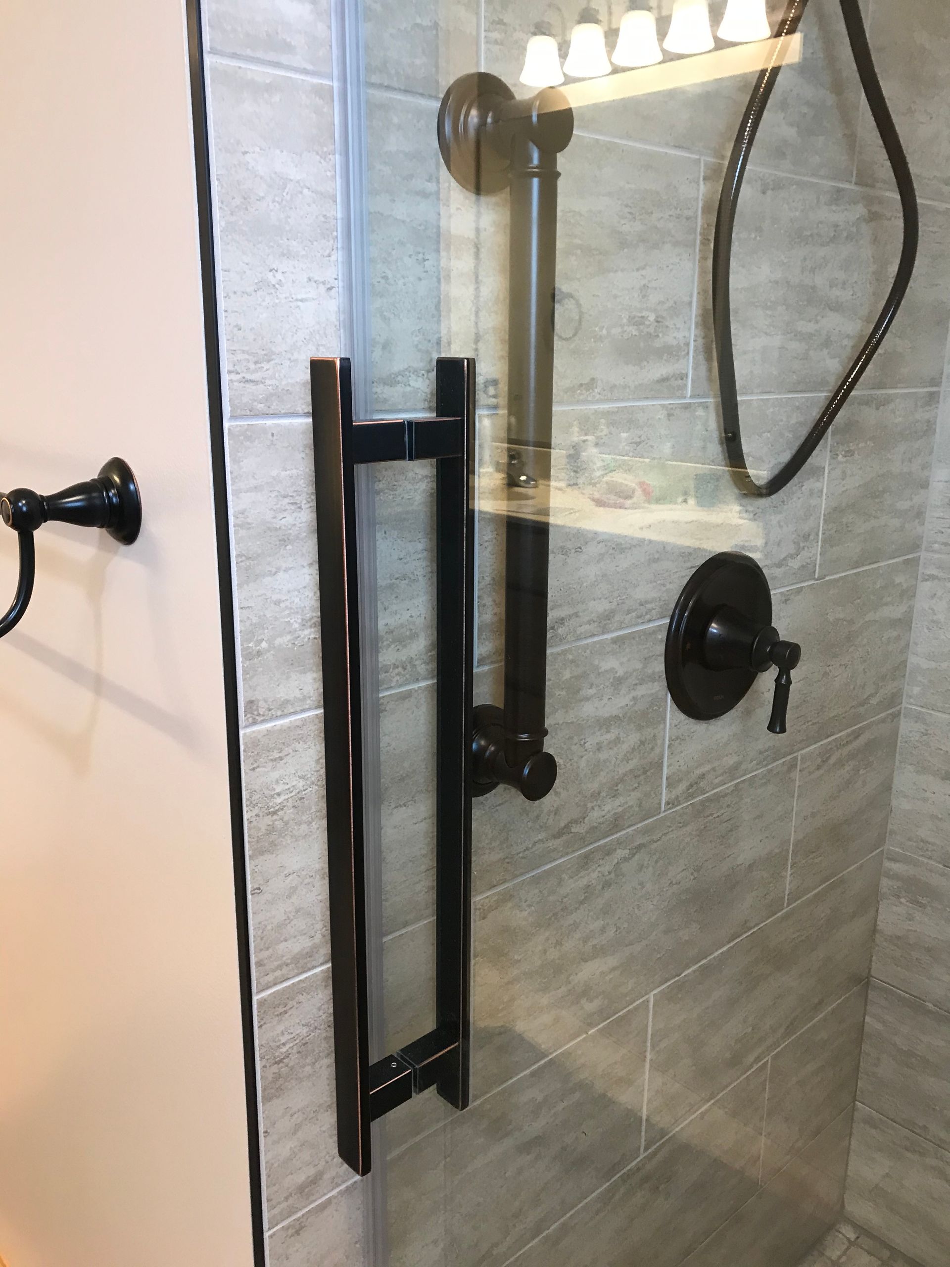 A modern shower with dark hardware, including a door handle and showerhead on a gray tiled wall.