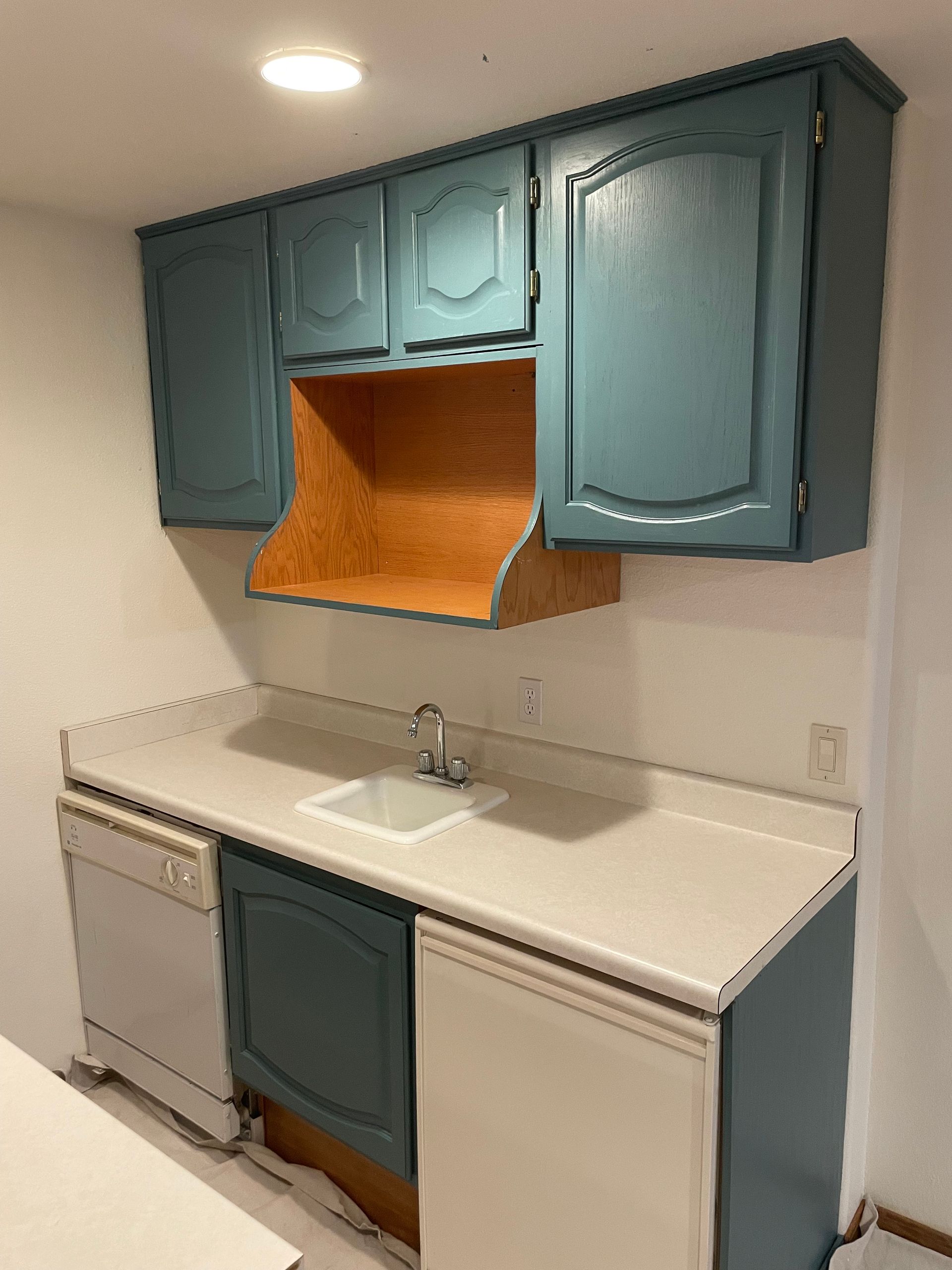 Blue kitchen cabinets, wood range hood, white countertops, and appliances.