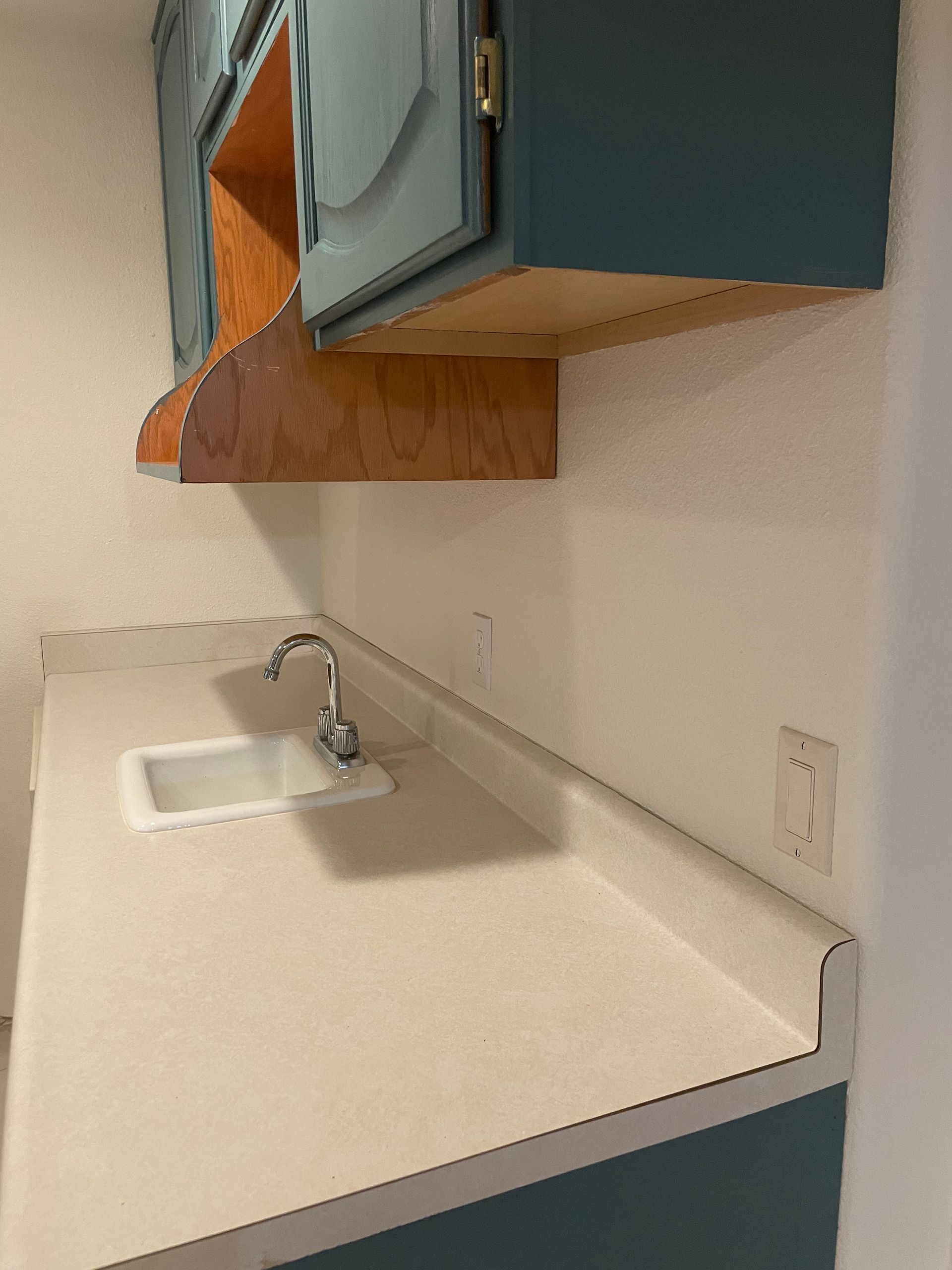 Small kitchen with blue cabinets, white countertop and sink.