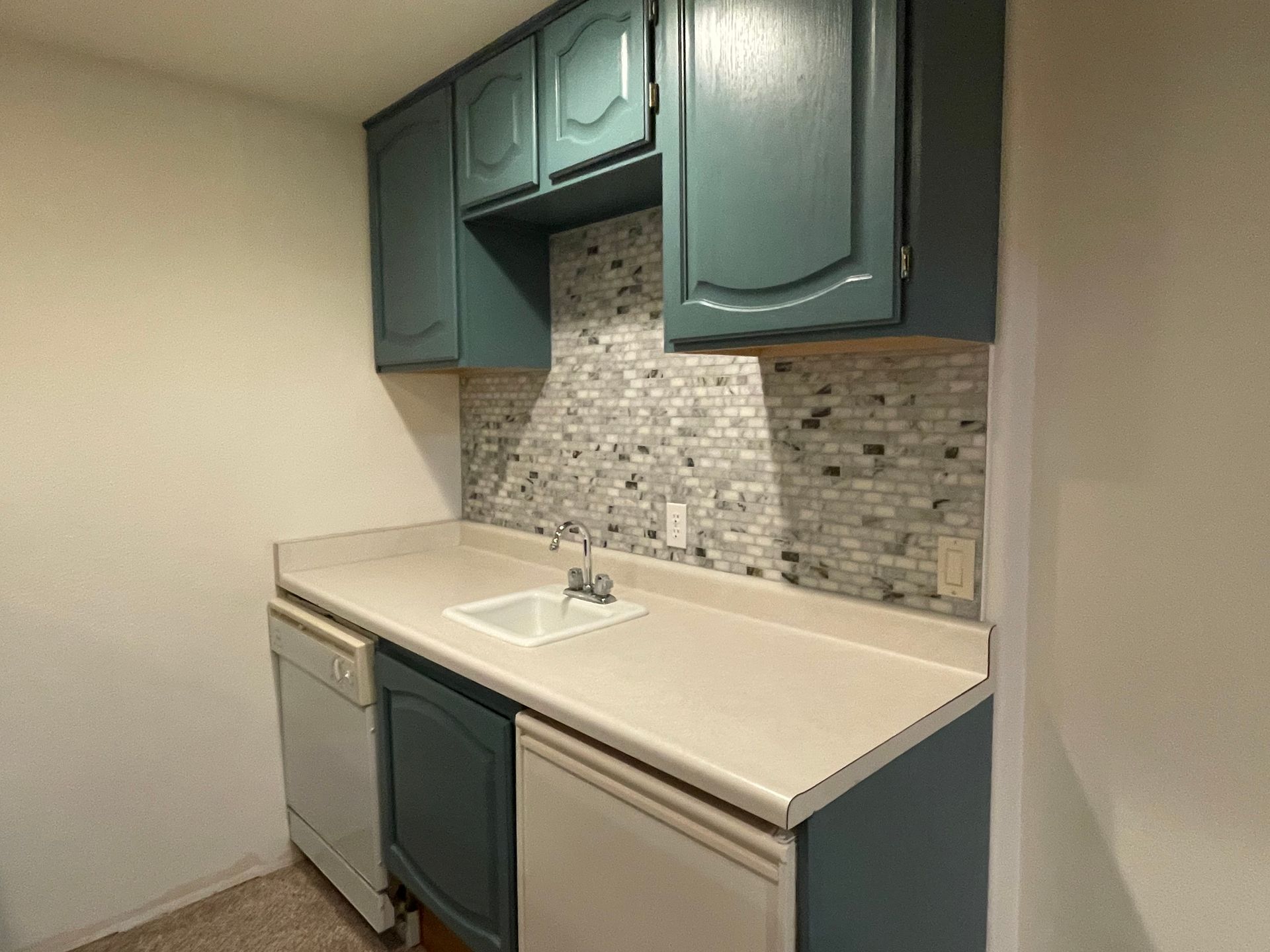 Small kitchen with teal cabinets, white countertop, mosaic backsplash, and a sink.