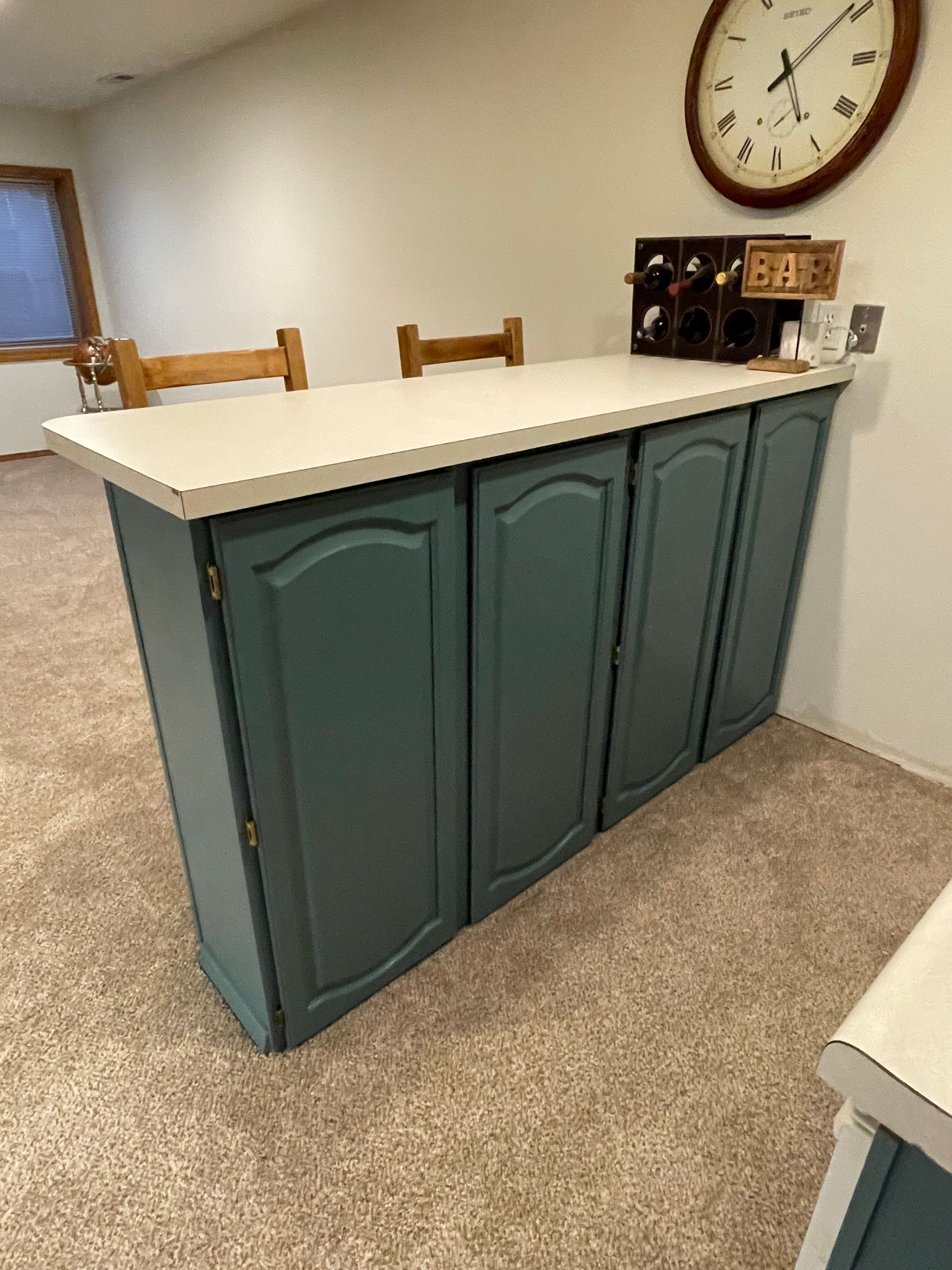 Blue cabinet bar with white countertop, two chairs, and a large clock on the wall.