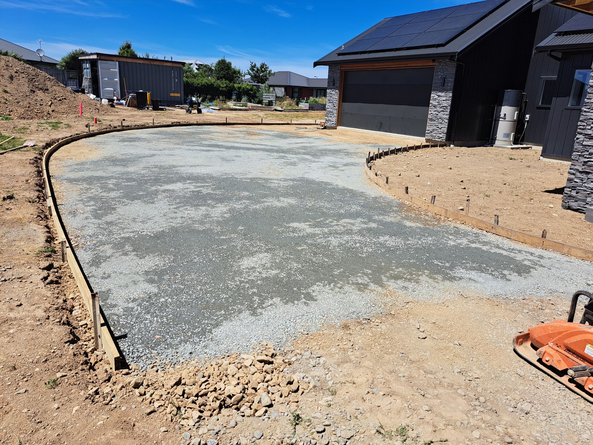 A residential driveway under construction with a leveled gravel base contained by wooden form boards in front of a house.