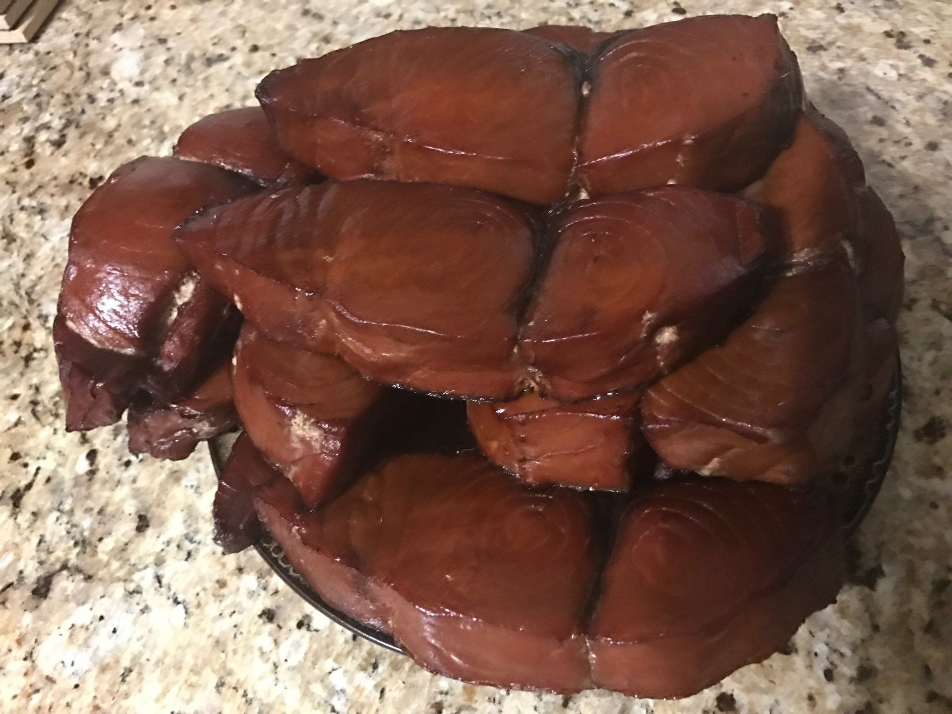 Pile of smoked tuna steaks, dark brown with a glossy finish, resting on a wire rack on a countertop.