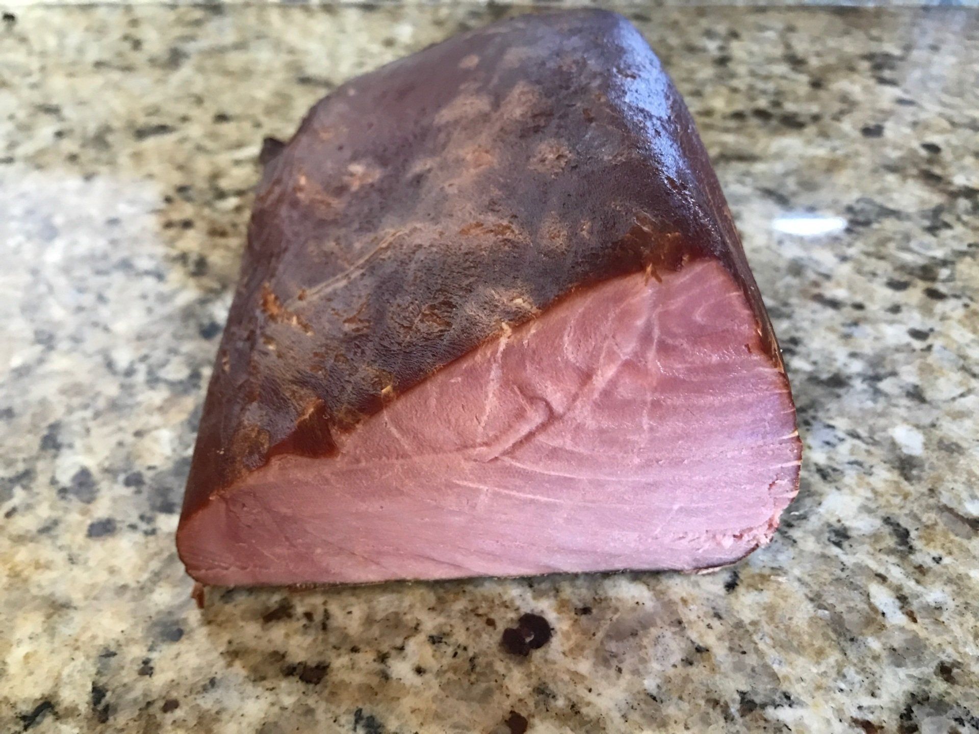 A block of cured tuna, pink flesh with a reddish-brown exterior, on a speckled countertop.